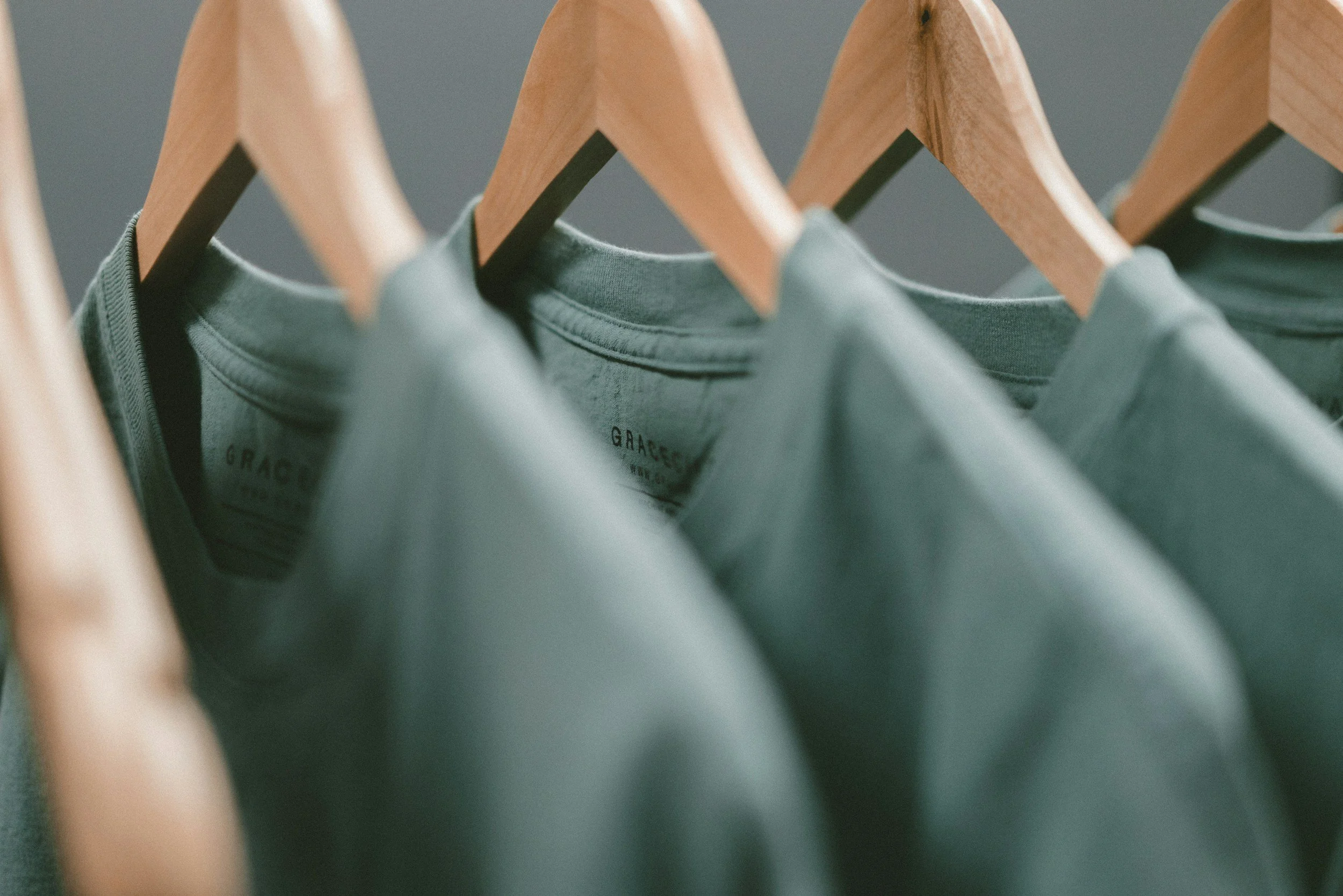 Green T-shirts hanging on wooden hangers on a clothing rack.