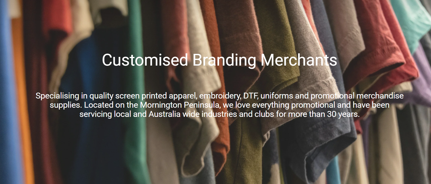Clothes in various colors hanging on a rack, with a text overlay about customized branding merchants specializing in screen printed apparel, embroidery, DTF, uniforms, and promotional merchandise.