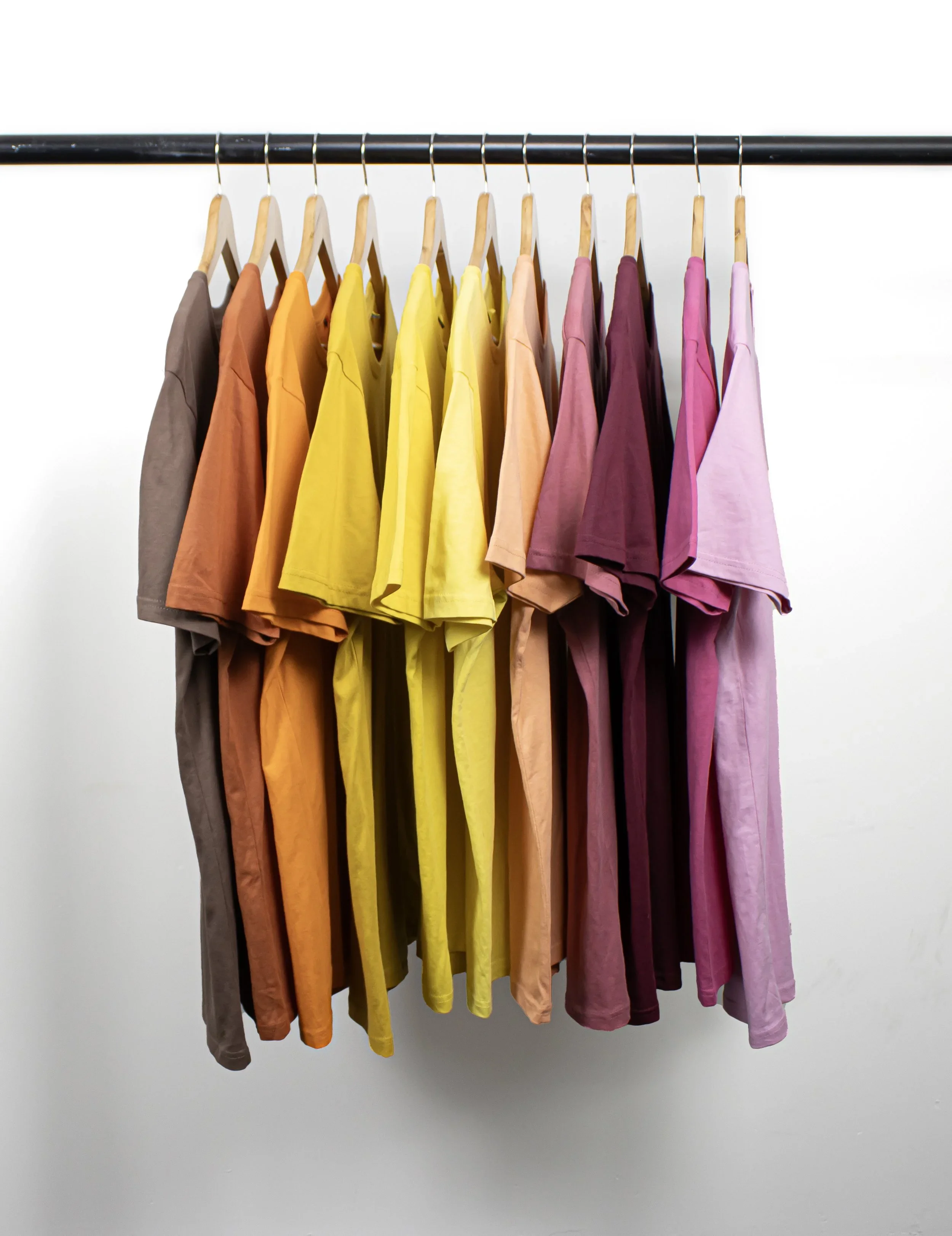 Clothes hanging on a black rod in a gradient color pattern from gray, orange, yellow, peach, maroon, pink, to purple.