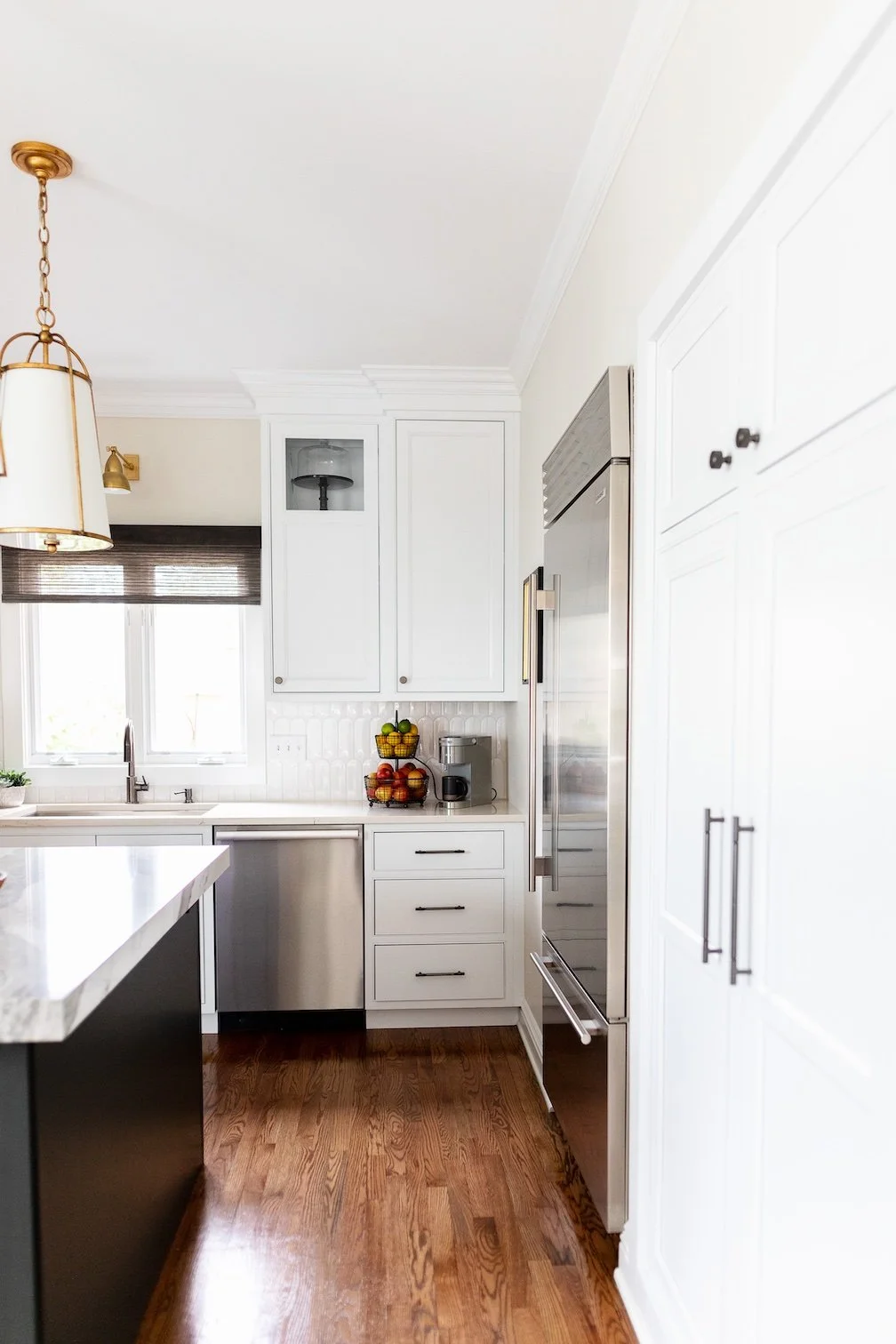 Modern kitchen with white cabinets, stainless steel appliances, granite countertop, wooden floor, and window with blinds.
