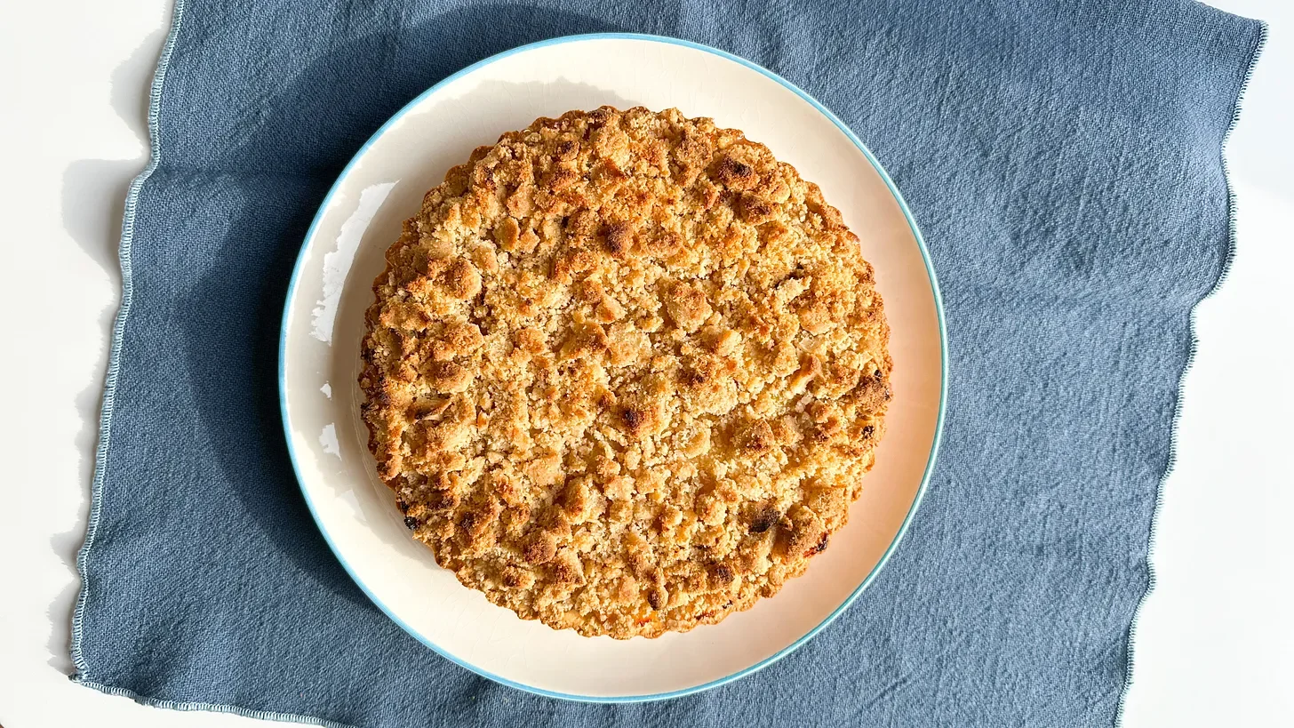 Photo of an apple crumble tart on a blue tablecloth.