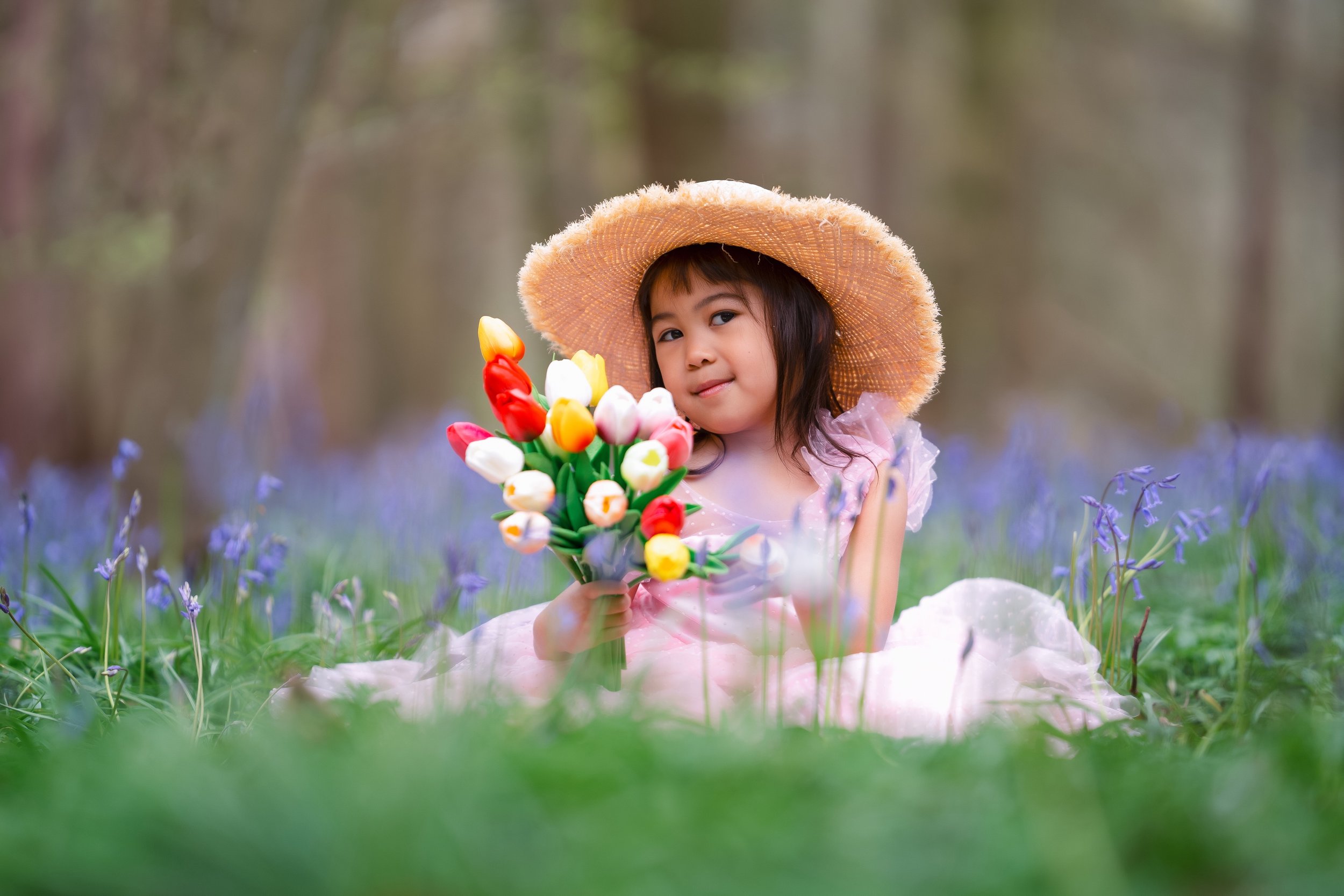 Little girl in pink dress sitting by the bluebells in the woods taken by Guildford photographer