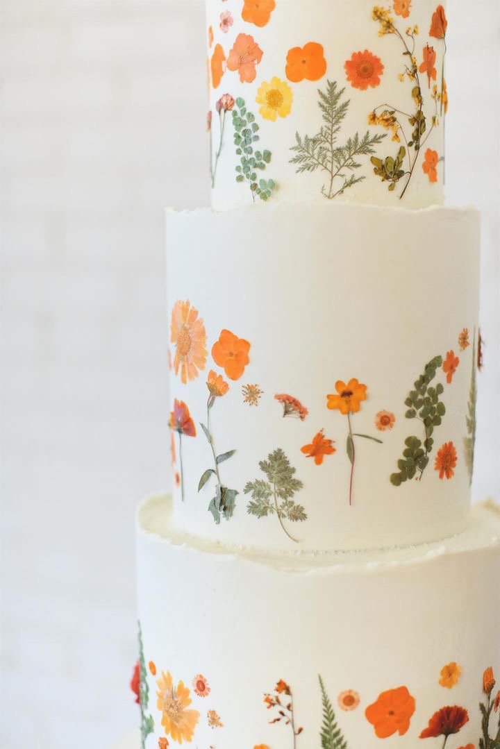 Three-tier white cake decorated with pressed orange and green flowers.