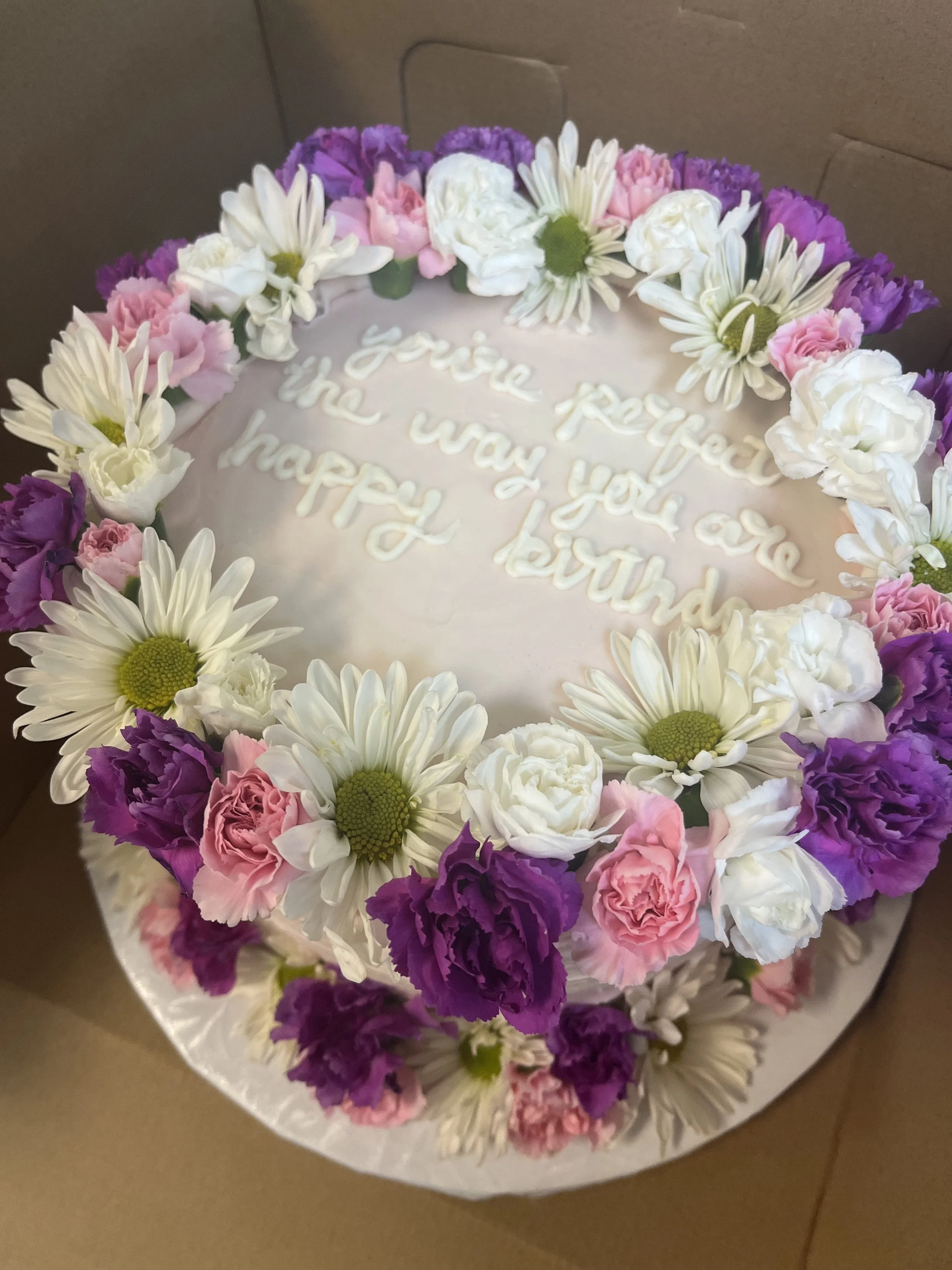 Pink and white flower arrangement on a cake with a message written in white icing.