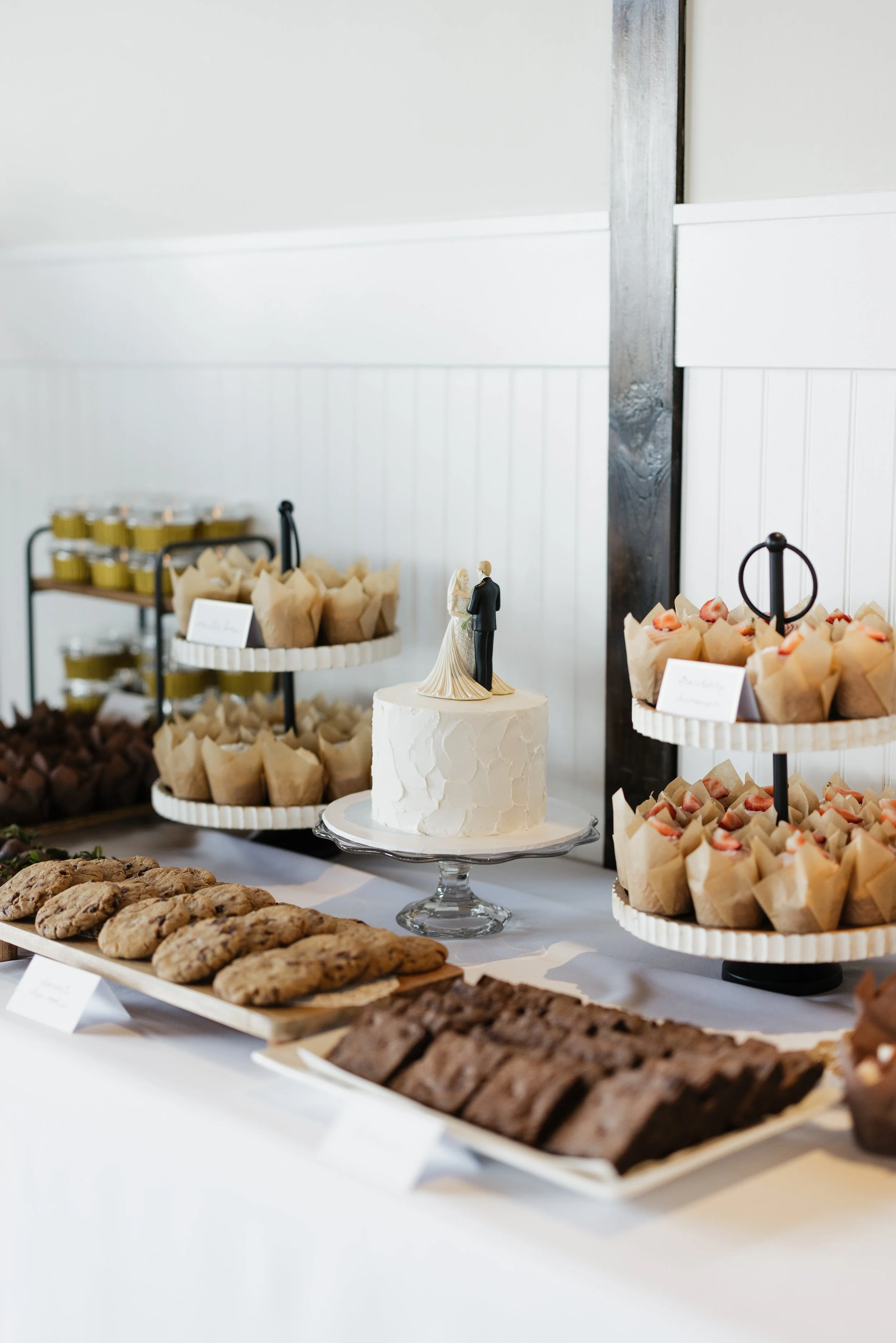 Wedding reception table with cookies, cupcakes, and a wedding cake topper featuring a bride and groom.