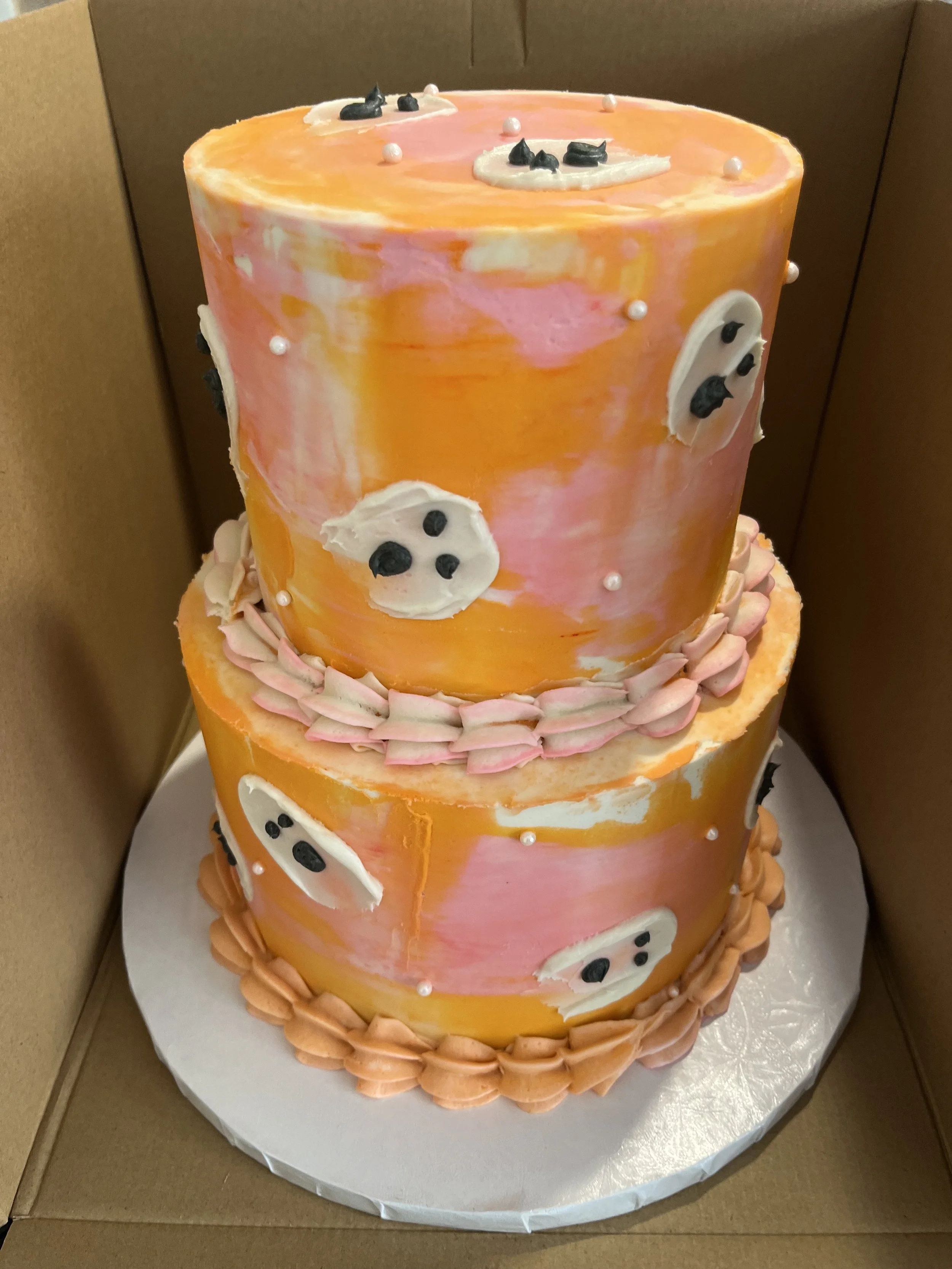 A two-tiered cake decorated with pink, orange, and white marbled icing, white icing faces with black eyes, and pink piped border at the base of the bottom tier.
