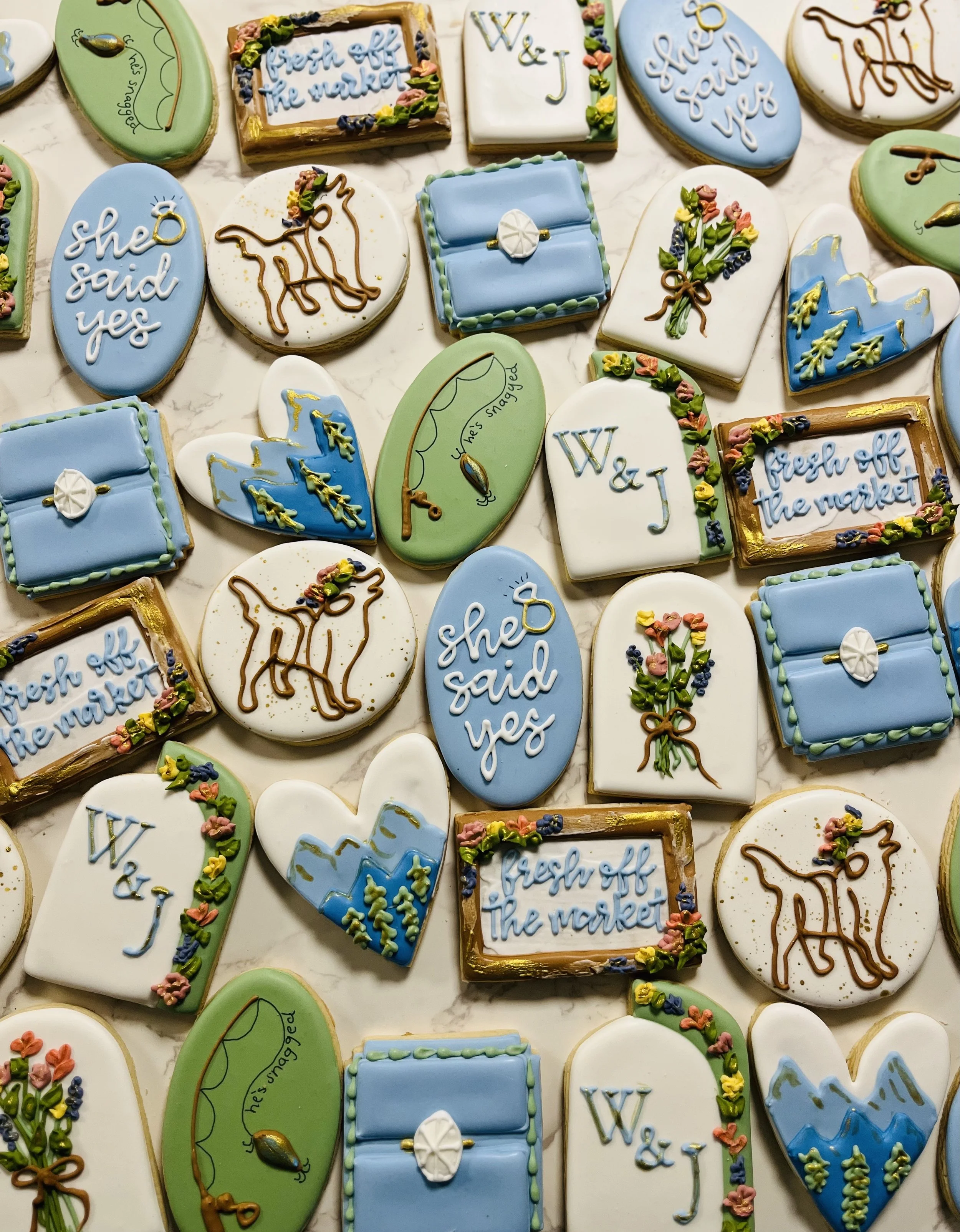Decorated cookies themed around the W&J (Washington and Jefferson) university or college. The cookies include cookies with the words 'she said yes', 'fresh off the market', and various designs like tennis rackets, and flowers, with some decorated with icing and gold accents.