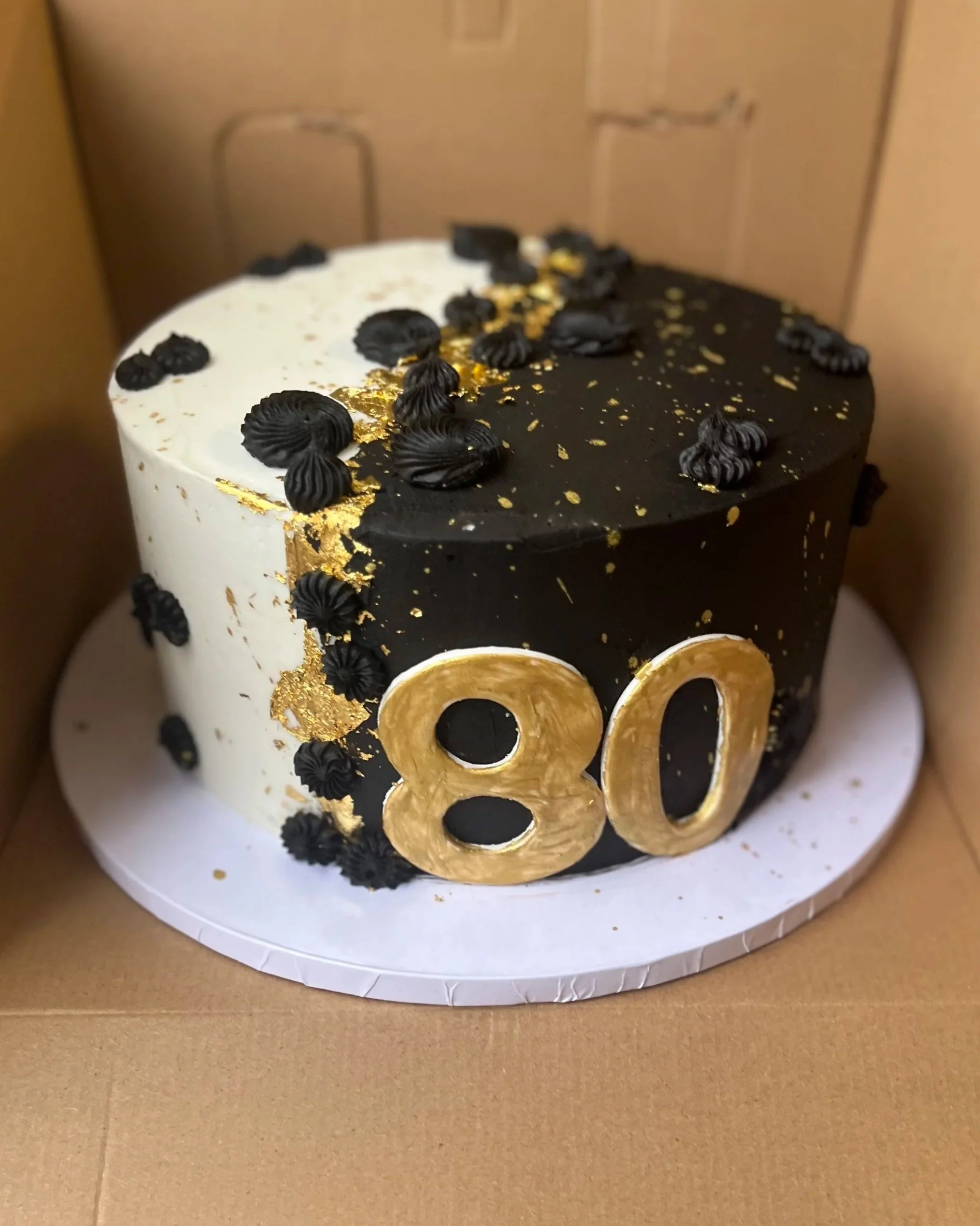 Half and half birthday cake with black, white, and gold decorations, displaying the number 80.