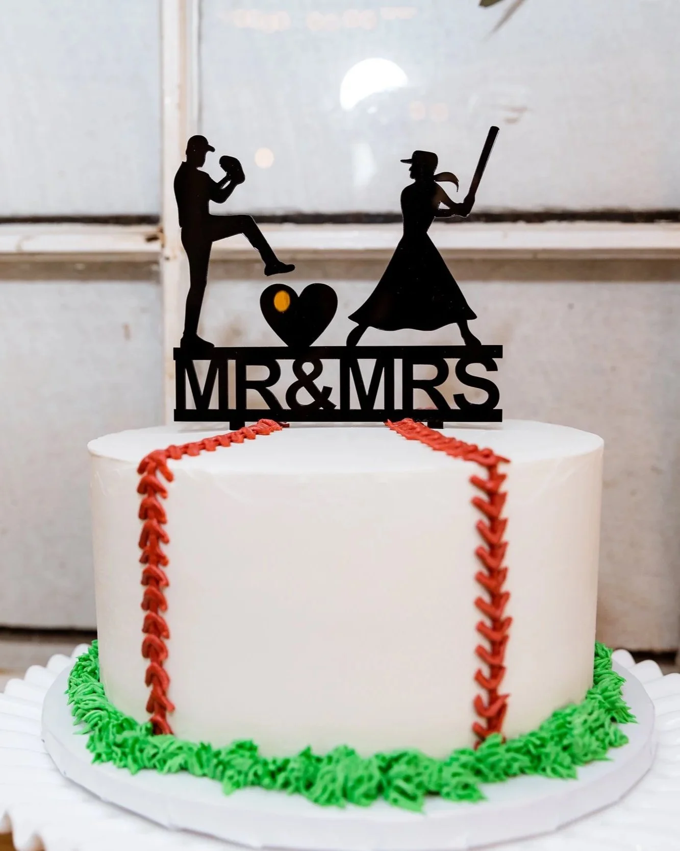 Wedding cake with a black topper featuring silhouettes of a man and woman, the man holding a baseball glove and the woman holding a bat, with the words 'Mr & Mrs' underneath.