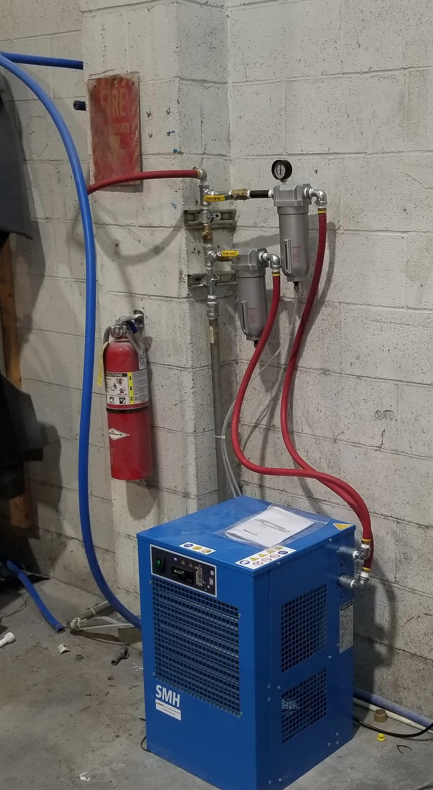 An industrial setup with a blue refrigerated air dryer, red Parker Pushlok and blue RapidAir hoses connected to air system filtration and bypass plumbing installed by The Compressor Guy, LLC.