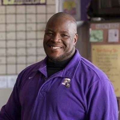 image of Wil Johnson, a black man with bald head, smiling, wearing a purple shirt