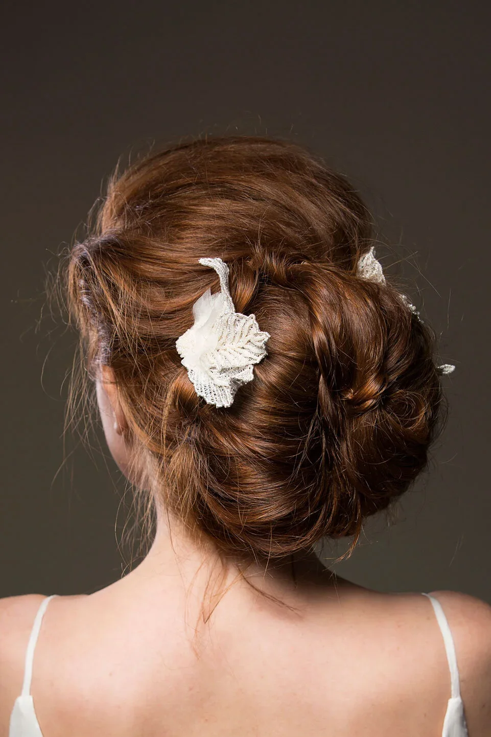 Updo hairstyle with white lace hair accessories on a woman with reddish-brown hair, wearing a white spaghetti strap top.