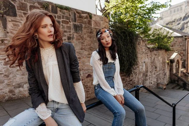 Promod 2018 collection - models sit together one is wearing dungarees and a head scarf the other is wearing a jacket, blouse and jeans
