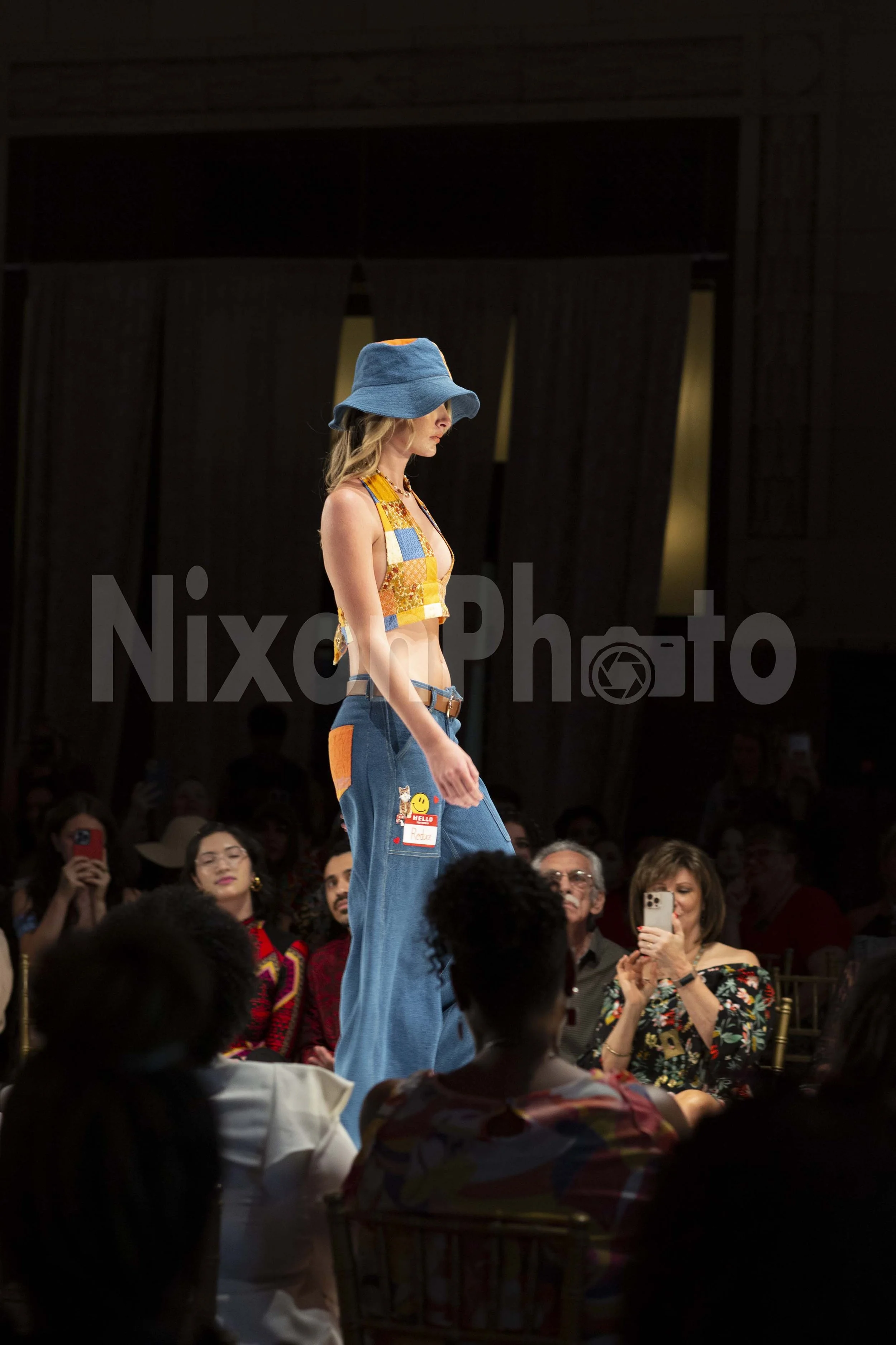 Fashion model wearing patchwork outfit and blue hat on runway