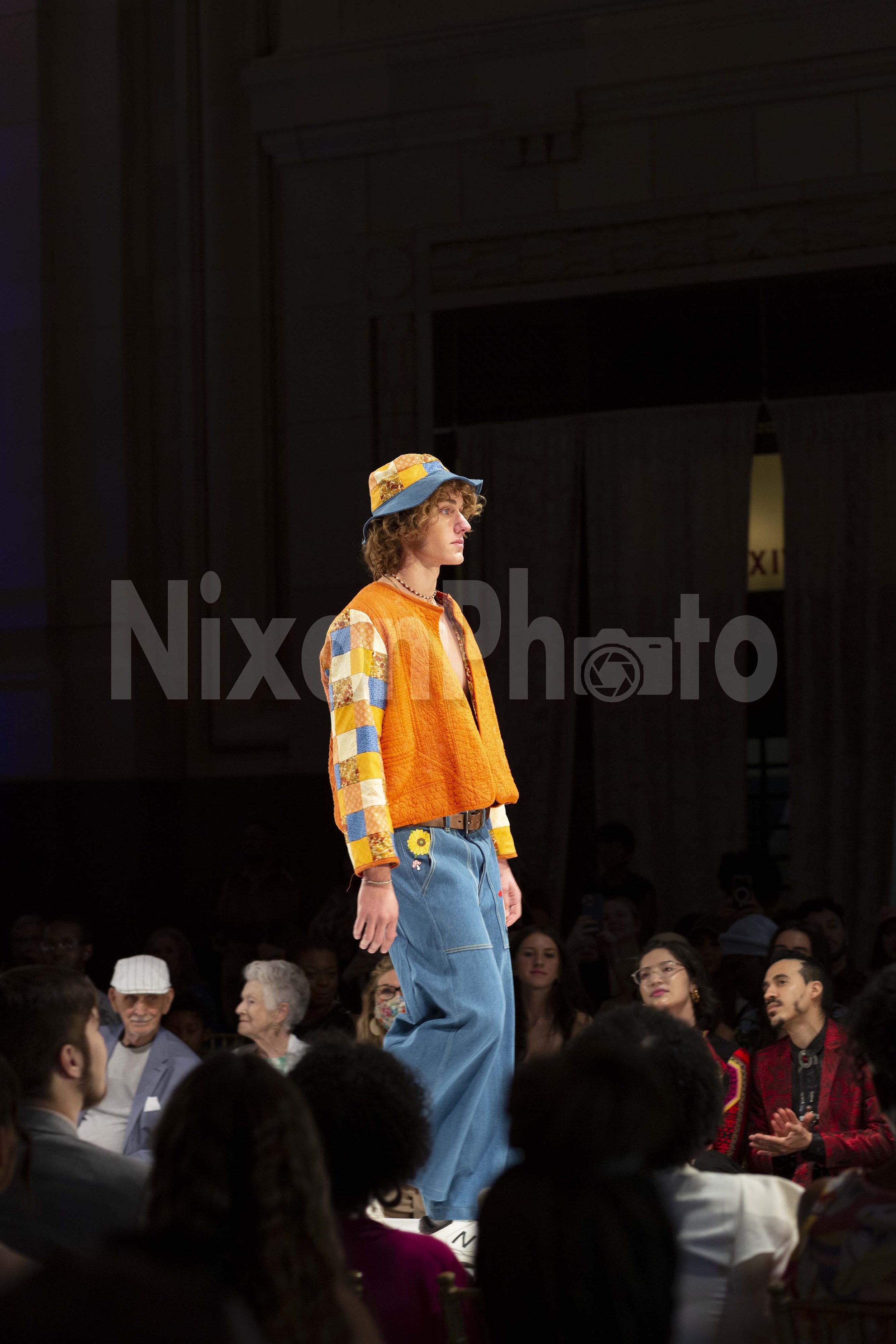 Model wearing colorful patchwork outfit on runway at fashion show.
