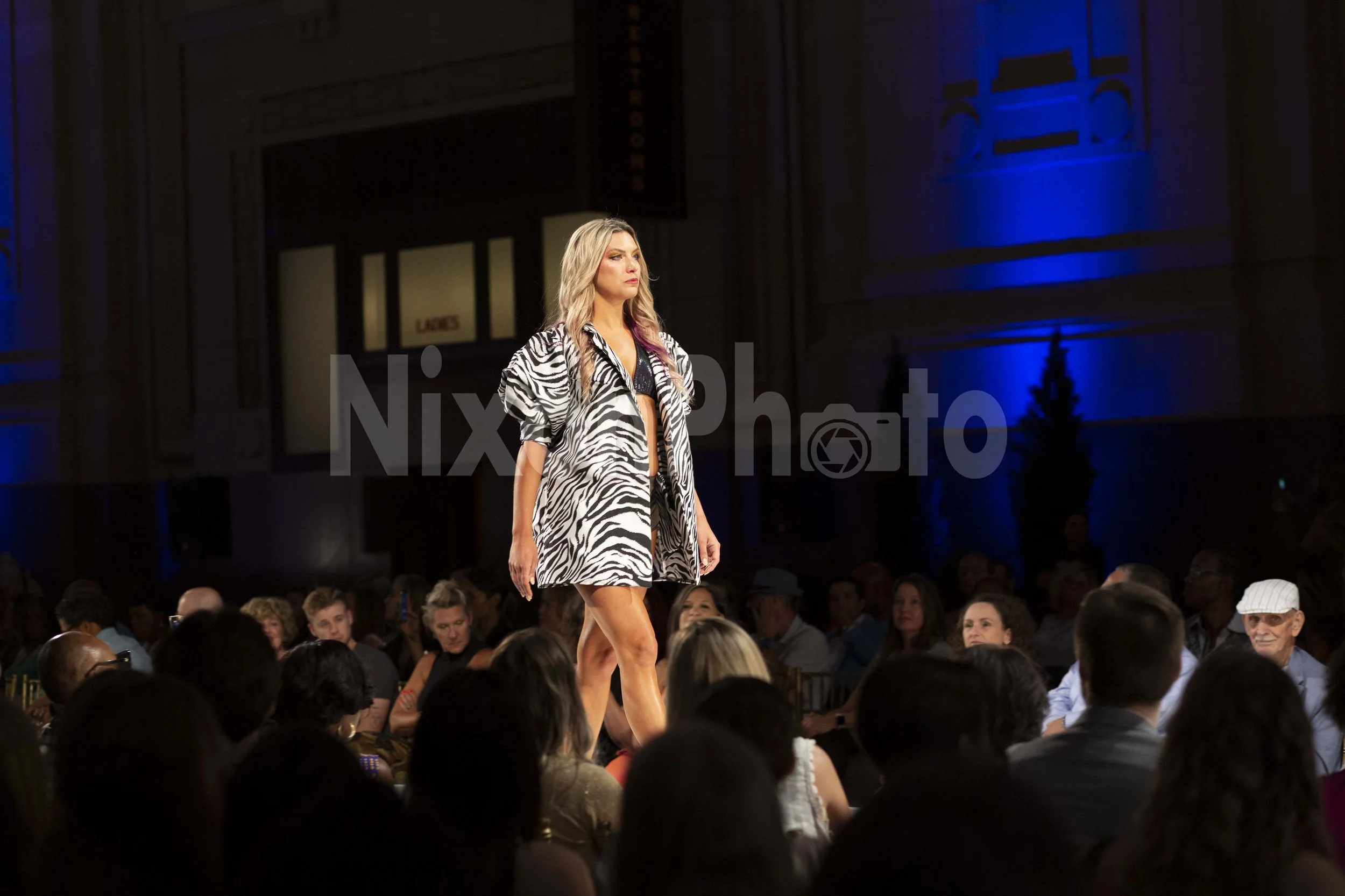 Fashion model walks runway in zebra print dress at fashion show.
