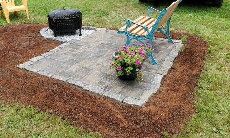 Paver patio with a bench and fire pit, bordered by mulch