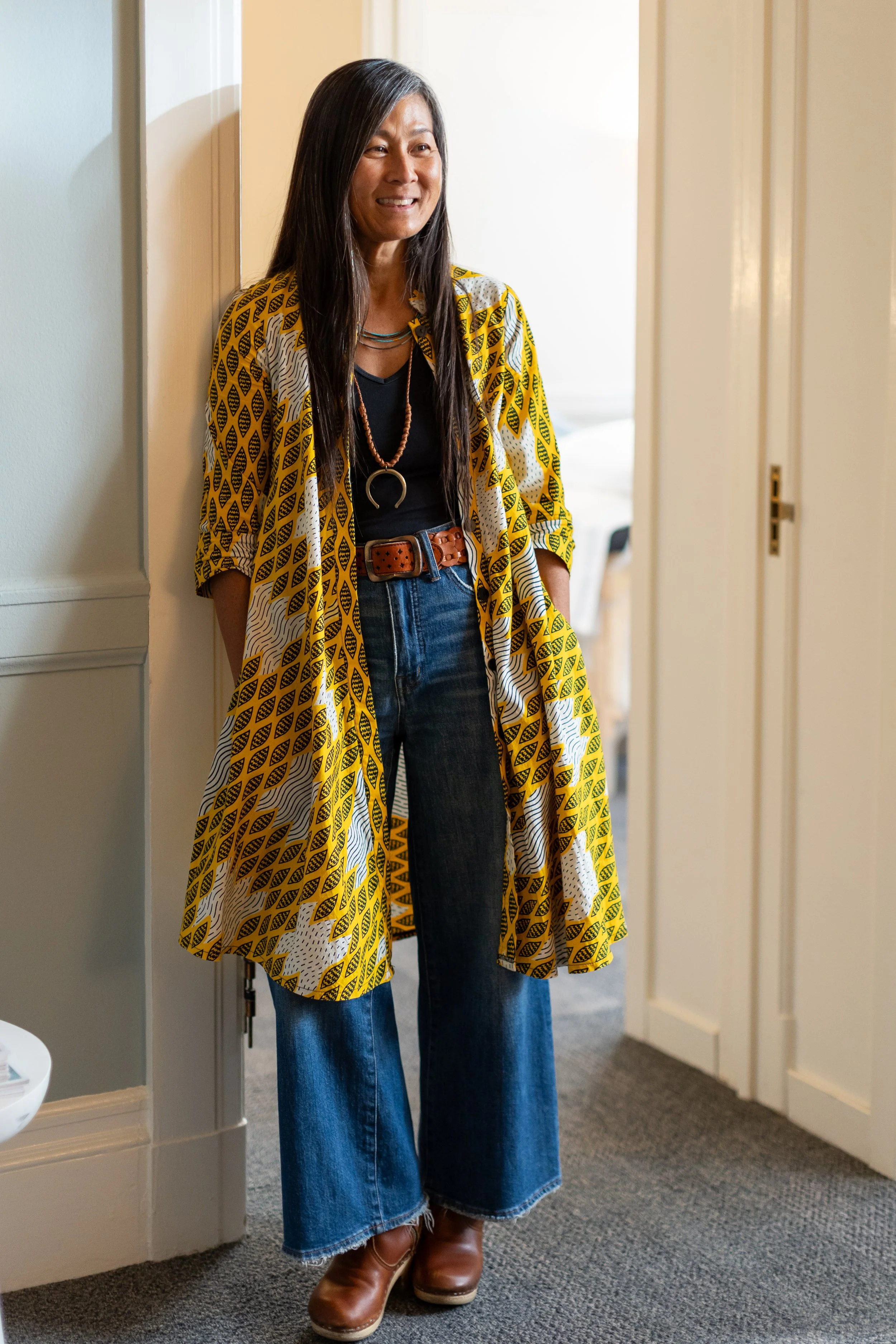 Michelle Kuroda, LAc, master acupuncturist in San Francisco, CA and Kailua-Kona, HI, specializing in nervous system regulation, neuromuscular re-education, embodied healing, and energy alignment smiling and standing in a doorway in her office.