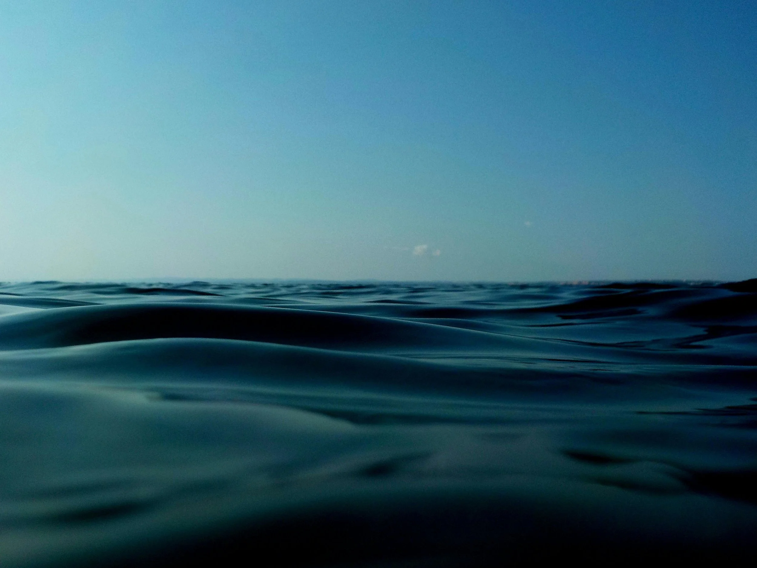 Photo of calm ocean waves under a clear blue sky.