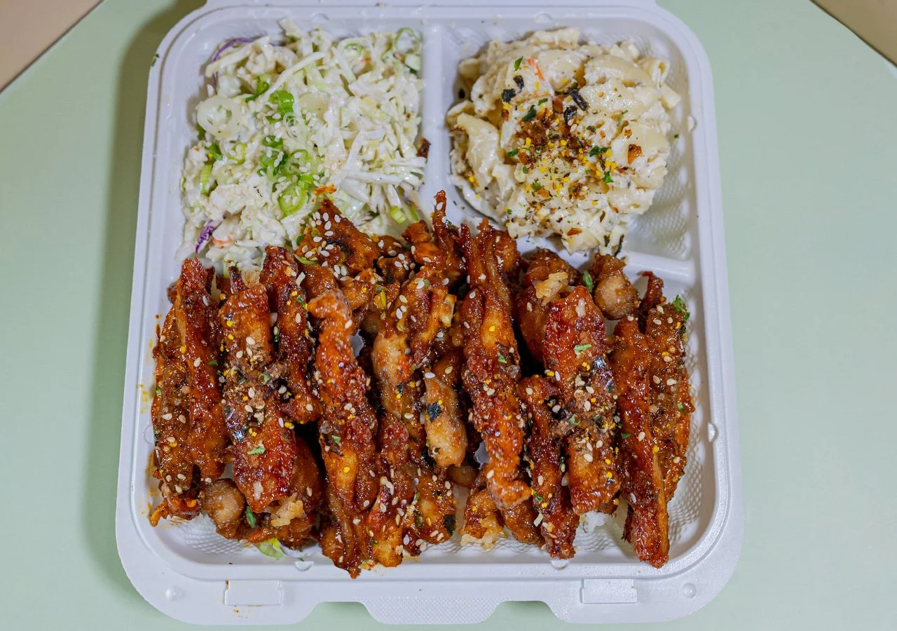 Single item plate of crispy fried chicken with soy glaze, garlic, and furikake served over white rice with sides of house slaw and macaroni salad.