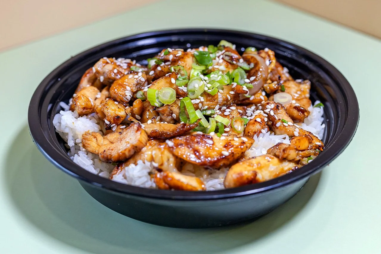 A bowl of pan-fried chicken coated in a sweet and savory soy-based teriyaki glaze, served over a bed of steamed rice.