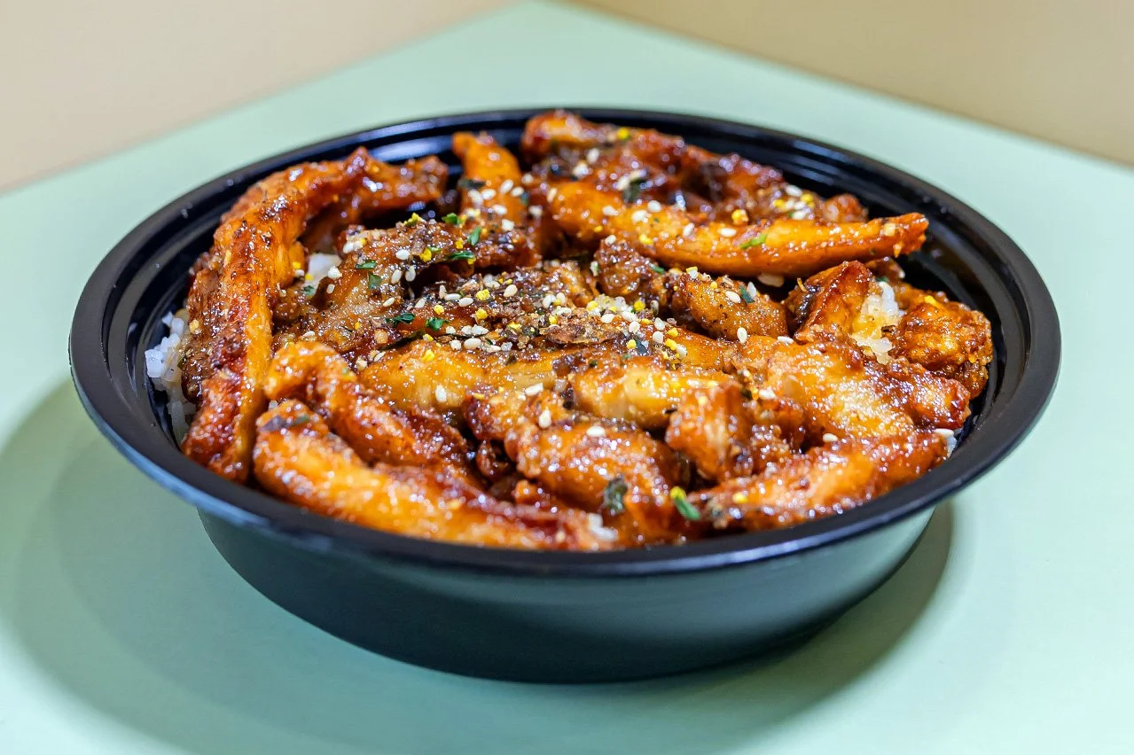 A bowl of crispy fried chicken with soy glaze, garlic, and furikake served with two scoops of white rice.
