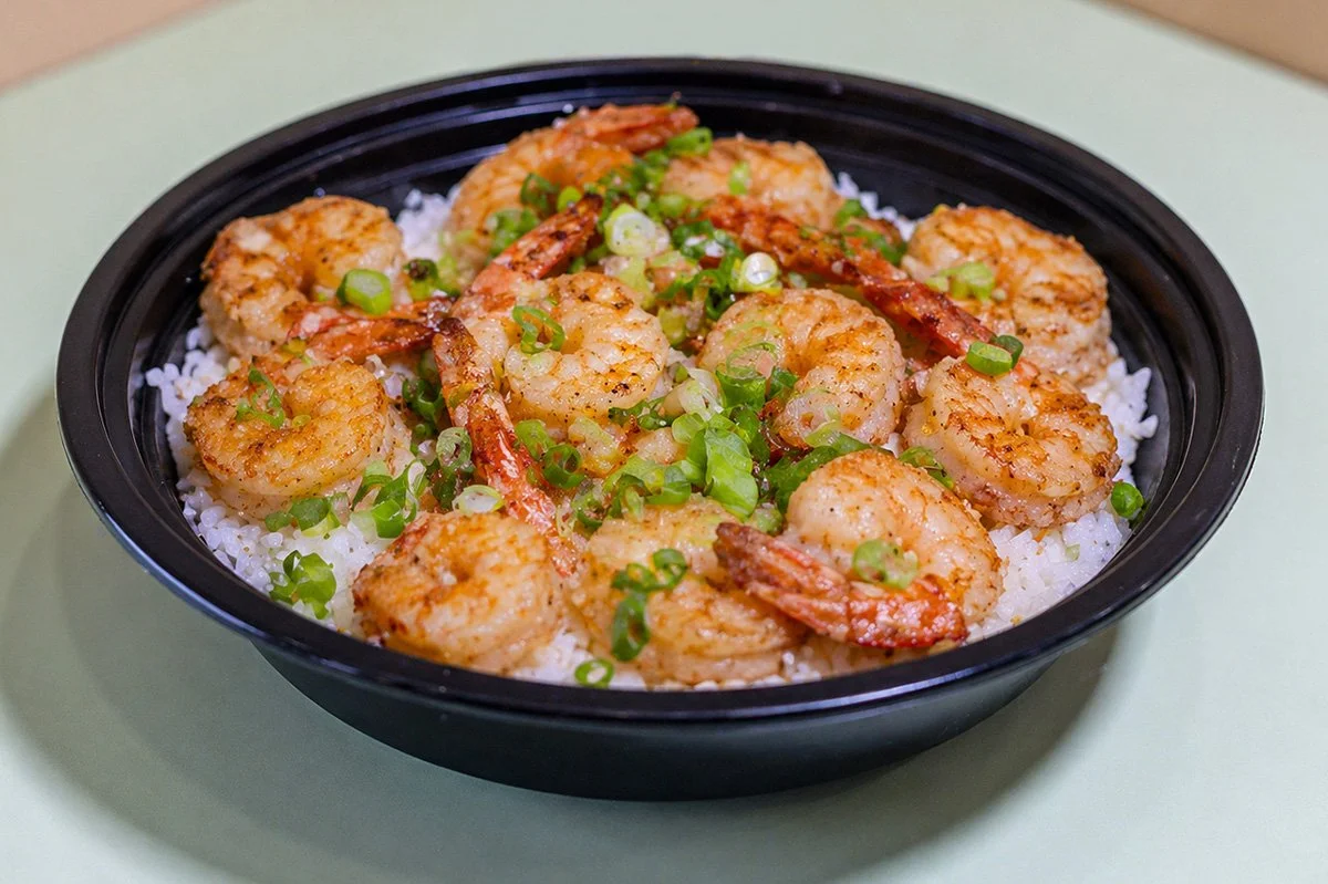 A bowl of Succulent shrimp pan-seared in rich butter and garlic served with two scoops of white rice