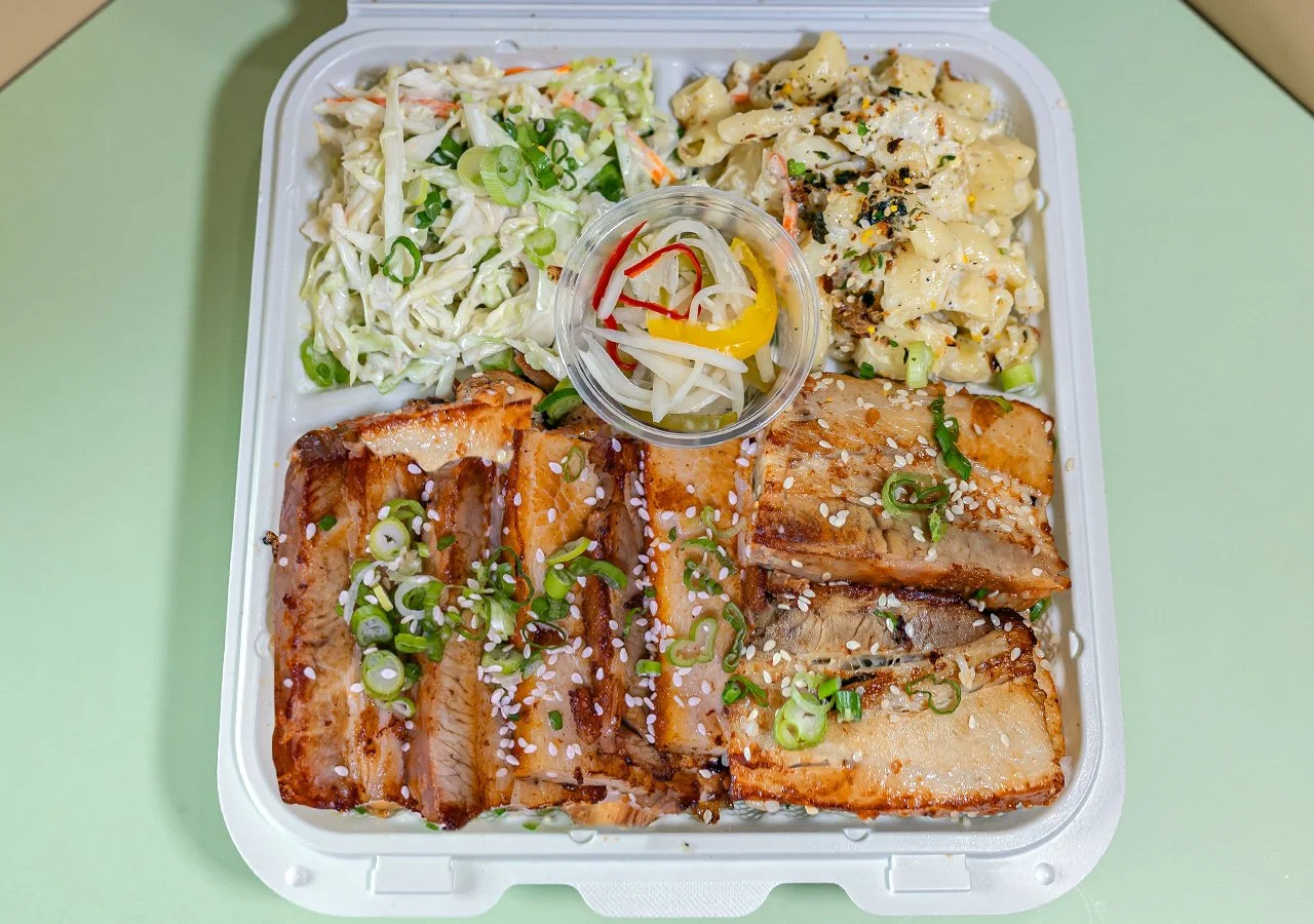 Single item plate of pork belly served over white rice with sides of house slaw and macaroni salad.