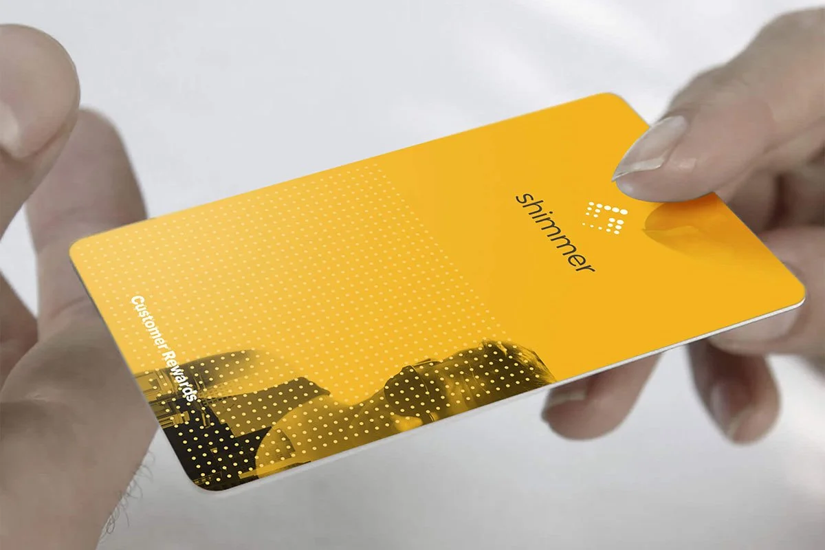 Close-up of a person holding a yellow Shimmer customer rewards card.