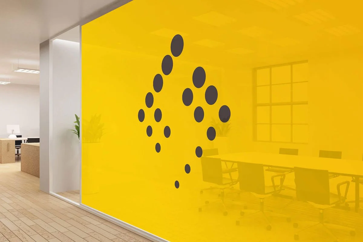 Kevin Schluter Design | Shimmer Branding | Application | Modern office with a yellow glass wall decorated with black circular decals, meeting room with chairs and table, and a workspace with a desk and computer.
