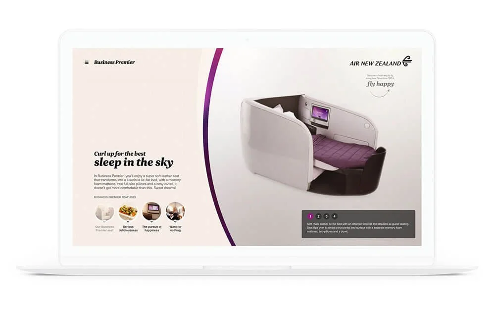 Air New Zealand Business Premier airline seat with entertainment screen, purple bedding, and privacy shell. The screen is turned on, displaying an interface.