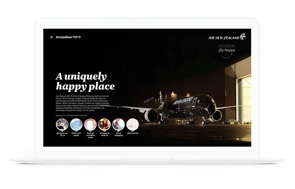 A white laptop displaying an airplane inside a hangar with the text "A uniquely happy place" and promoting Air New Zealand's Dreamliner 787-9 aircraft.
