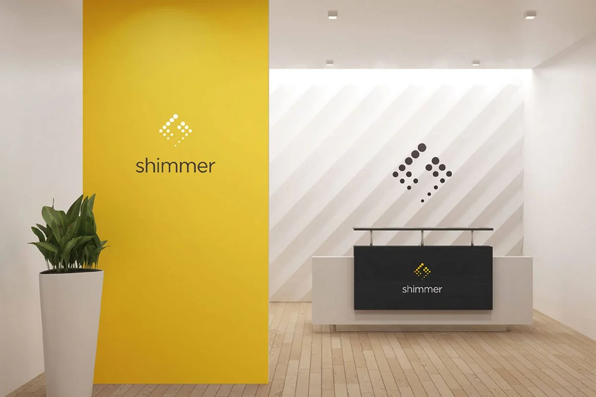 Kevin Schluter Design | Shimmer Branding | Application | Reception desk in a modern office with walls decorated with the word "shimmer" and abstract logo designs, a large potted plant, and a bright yellow accent wall.