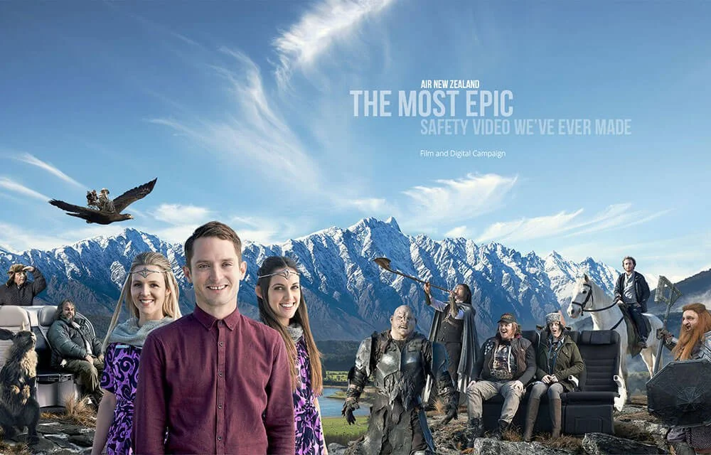 A promotional poster for Air New Zealand's safety video, featuring a fantasy adventure scene with people and characters in a scenic mountainous landscape, including a man and woman smiling at the front, a knight on horseback, and various mythical creatures.