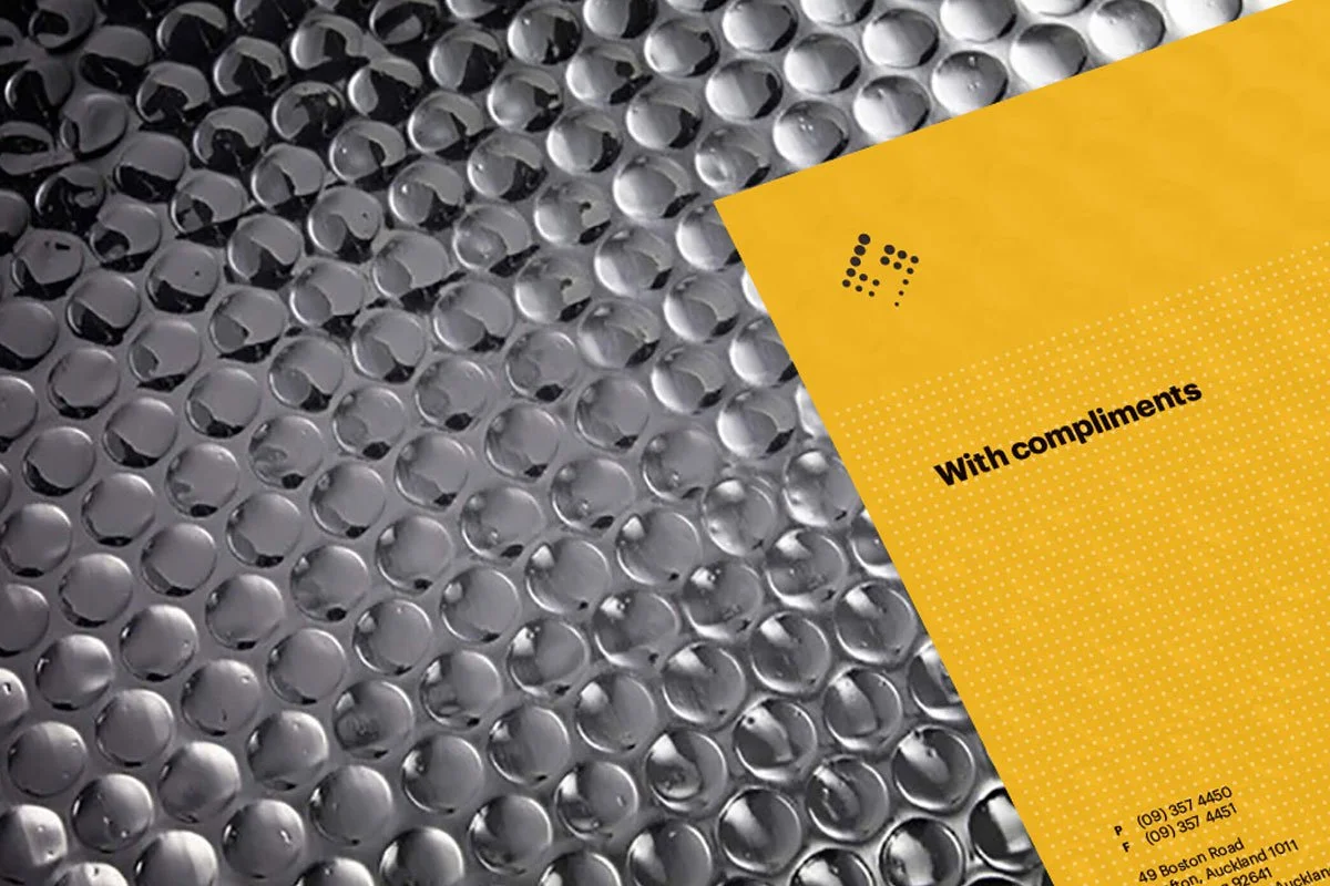 Kevin Schluter Design | Shimmer Branding | Application | Close-up of a sheet of metallic bubbles or blisters, possibly a bubble wrap, with a yellow overlay featuring black text that reads 'WITH COMPLIMENTS' and a phone and fax number.