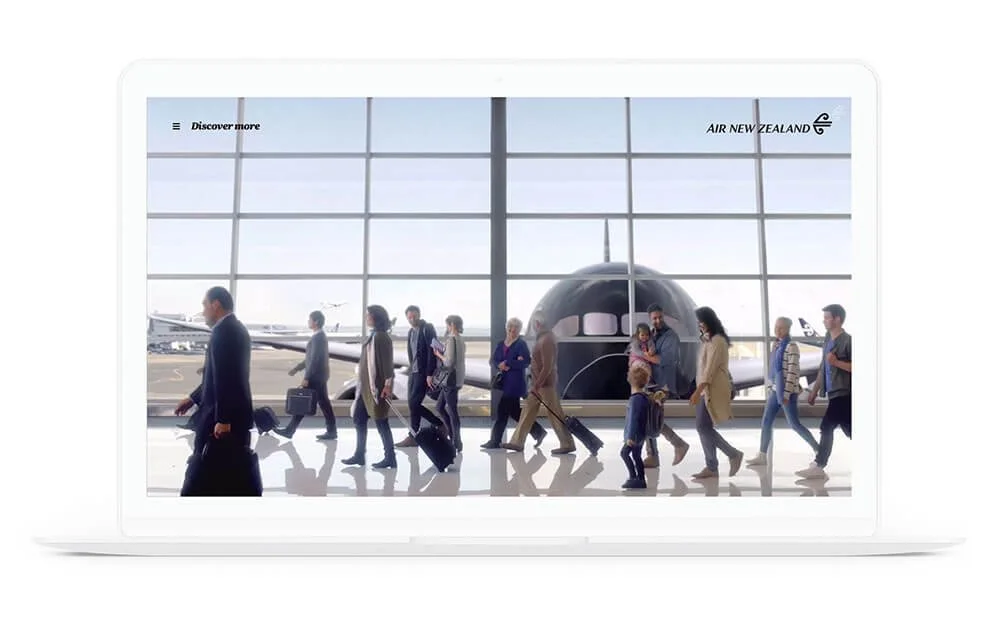 Passengers walking through an airport terminal with a large glass window showing airplanes outside, with Air New Zealand branding in the top right corner.