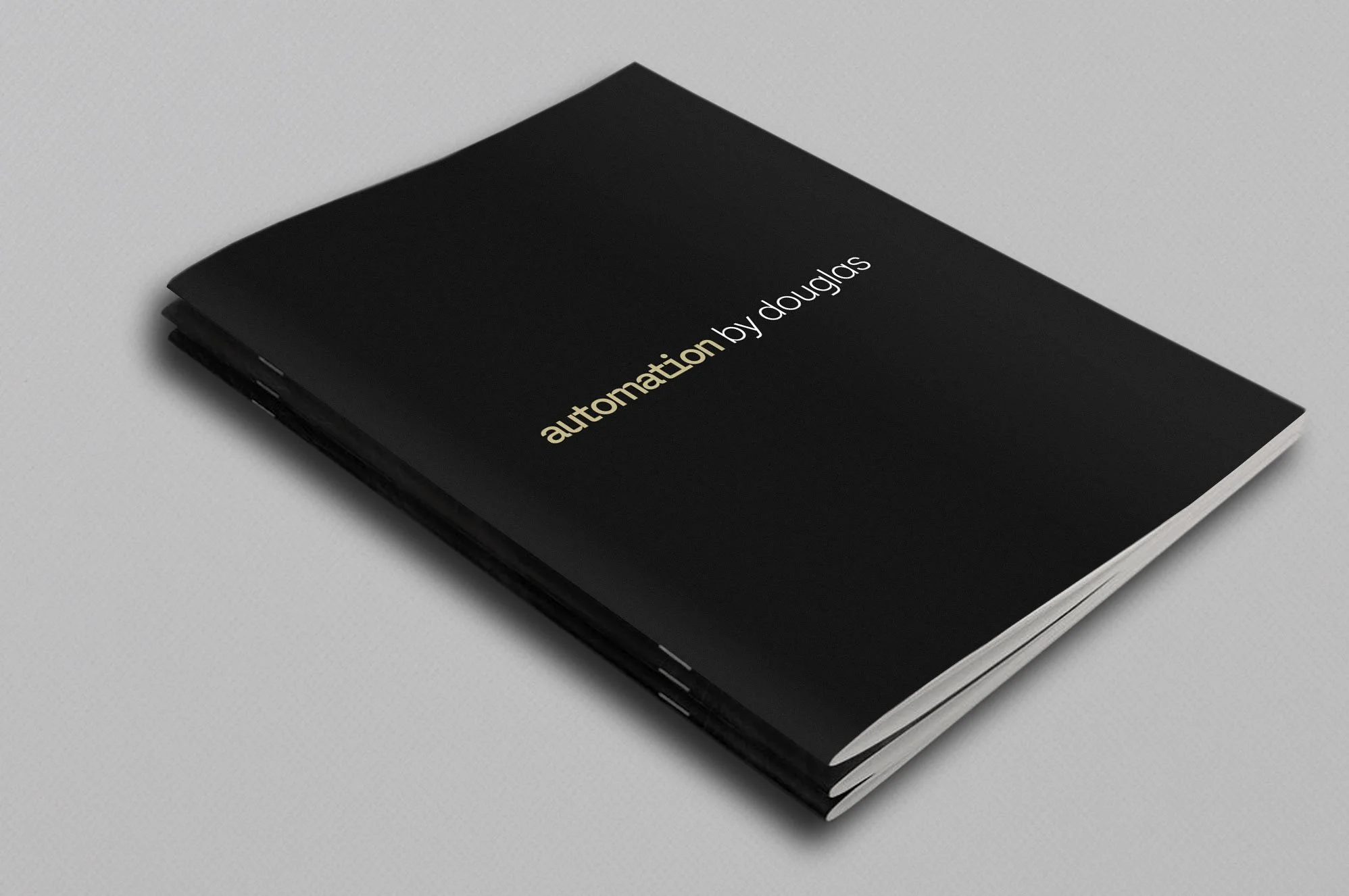 Kevin Schluter Design | Automation by Douglas | Service Design | A black booklet with the words "automation by douglas" in white and gold text on the cover, lying on a white surface.