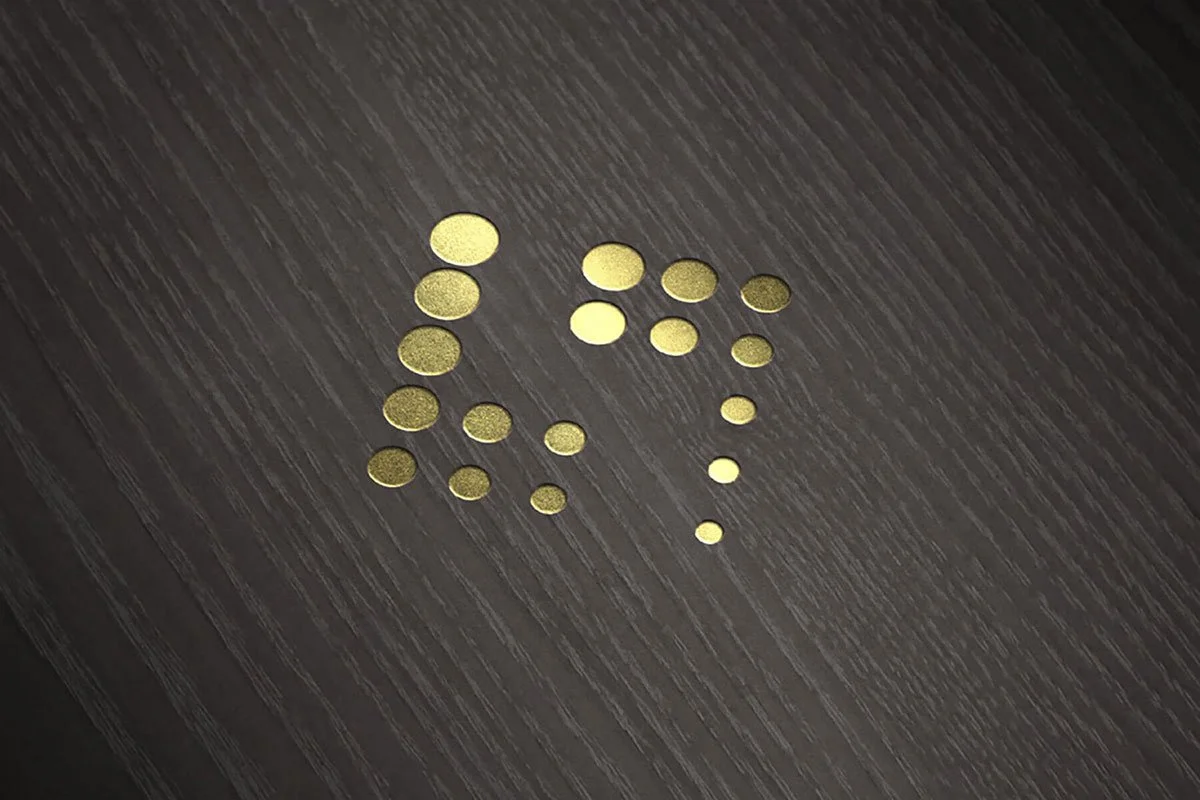Kevin Schluter Design | Shimmer Branding | Application | Small gold-colored round confetti scattered on a dark wooden surface.