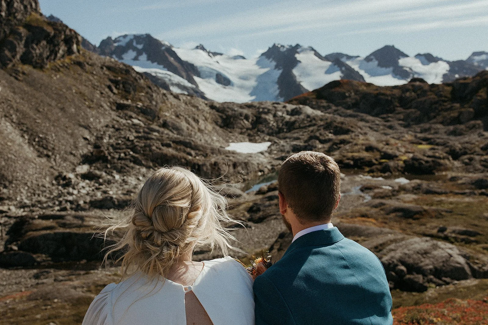 a coulpe looking out to an alskan Mountain range after their adventure, helicopter elopement, taking out of Seward Alaska