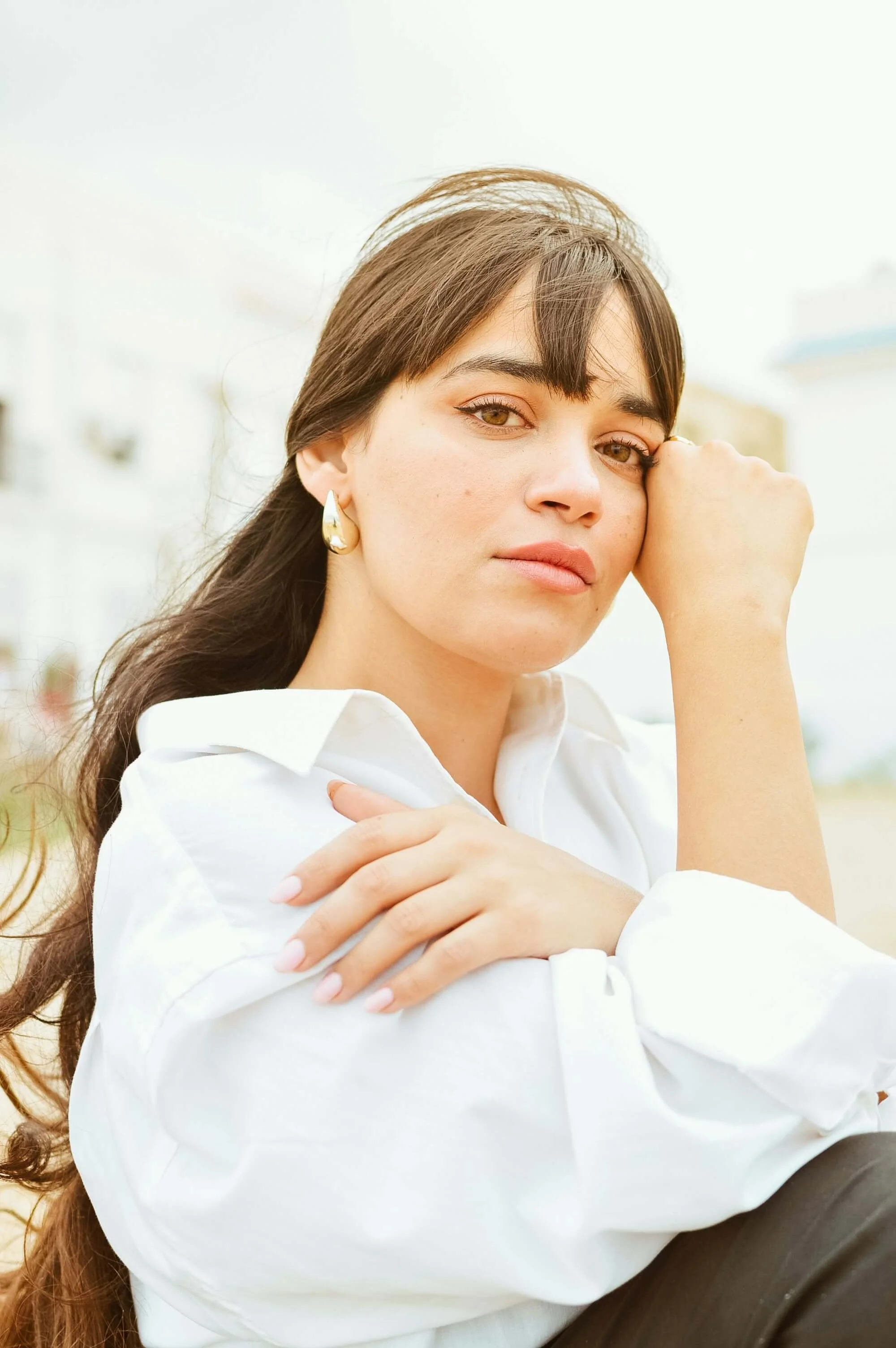 Brown-haired woman wearing gold earrings and white shirt, sitting outdoors with peaceful gaze | therapist for women in California.