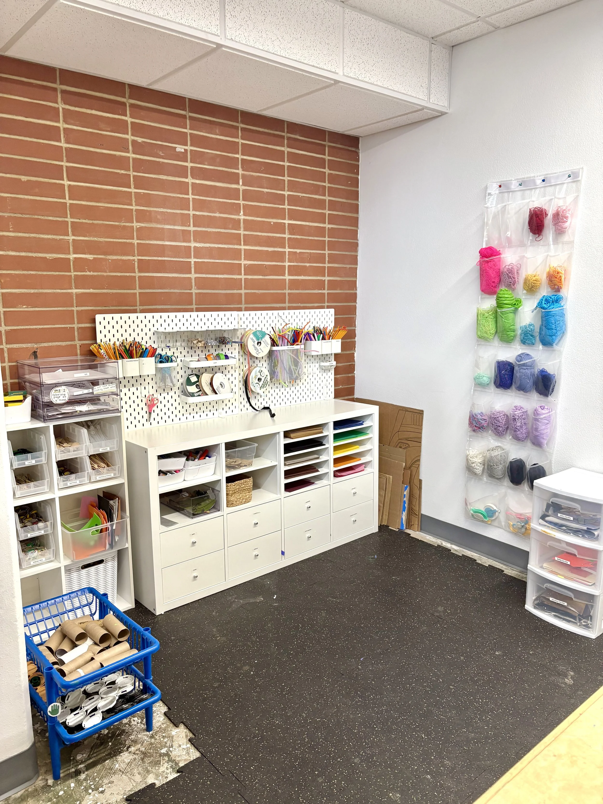 Organized craft room with storage bins, pink and blue yarn, and supplies for crafting or sewing.
