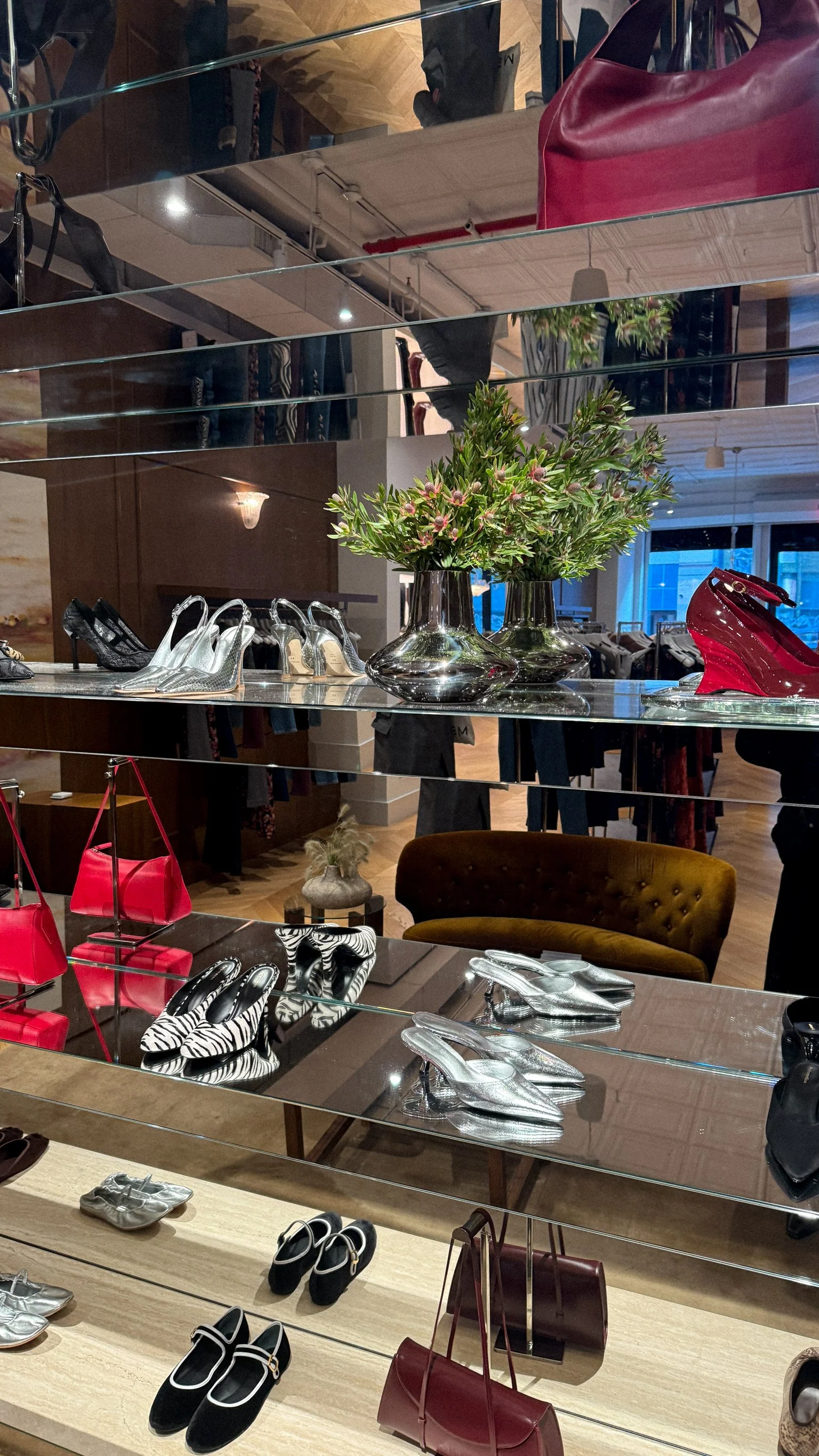 Display of women's shoes and handbags in a store, with decorative vases and a chair in the background.