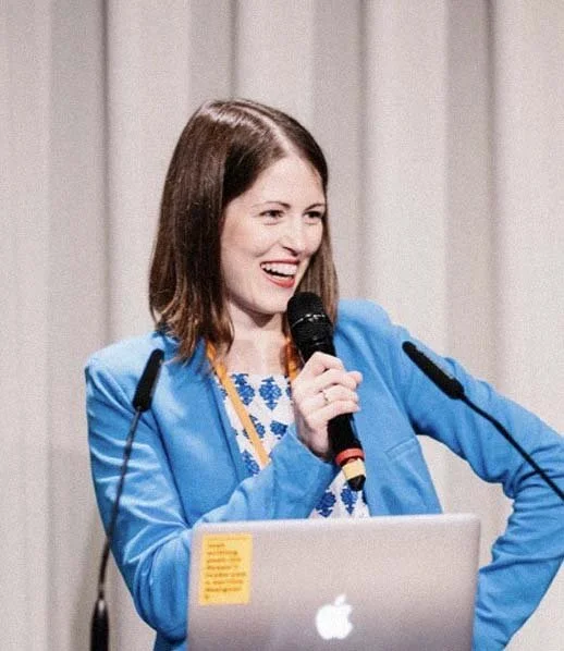 Portrait von Katrin Dribbisch im blauen Blazer mit einem Mikrofon lachend