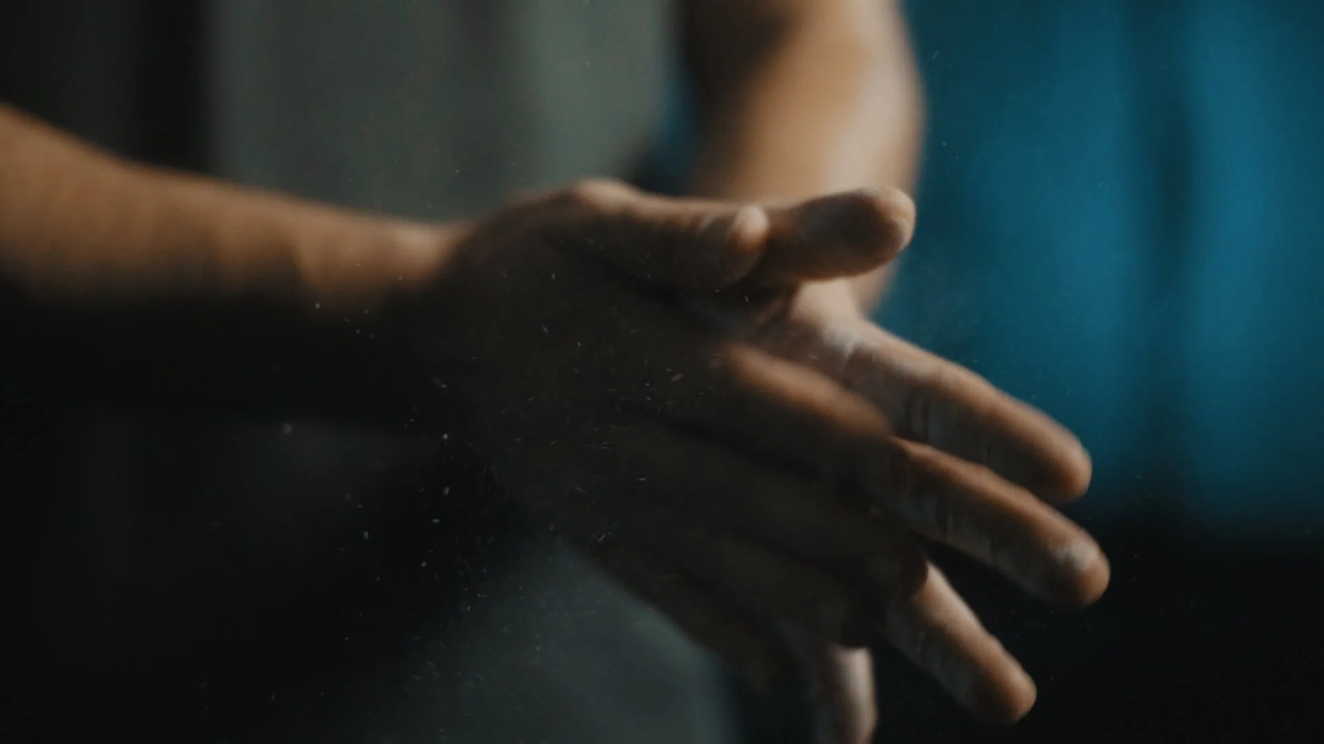 Close-up of a person's hand with fingers extended, dust or powder particles in the air, and a blurred background.