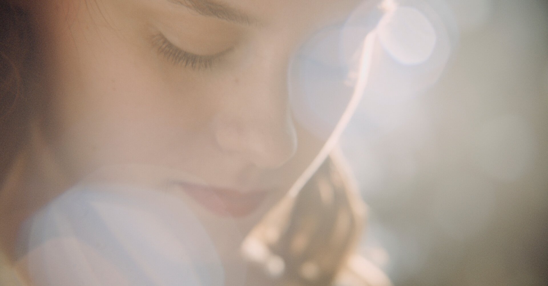 Close-up of a person's face with closed eye and makeup, illuminated by bright light creating a lens flare.
