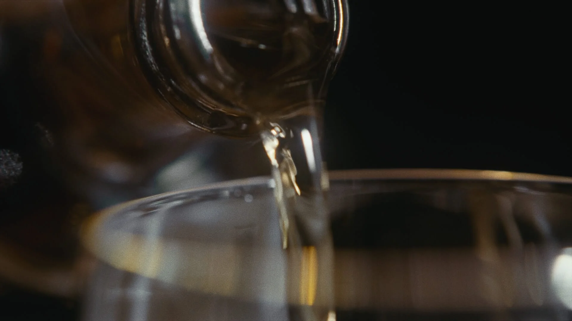 Pouring a dark liquid, likely coffee, from a glass bottle into a metal cup.