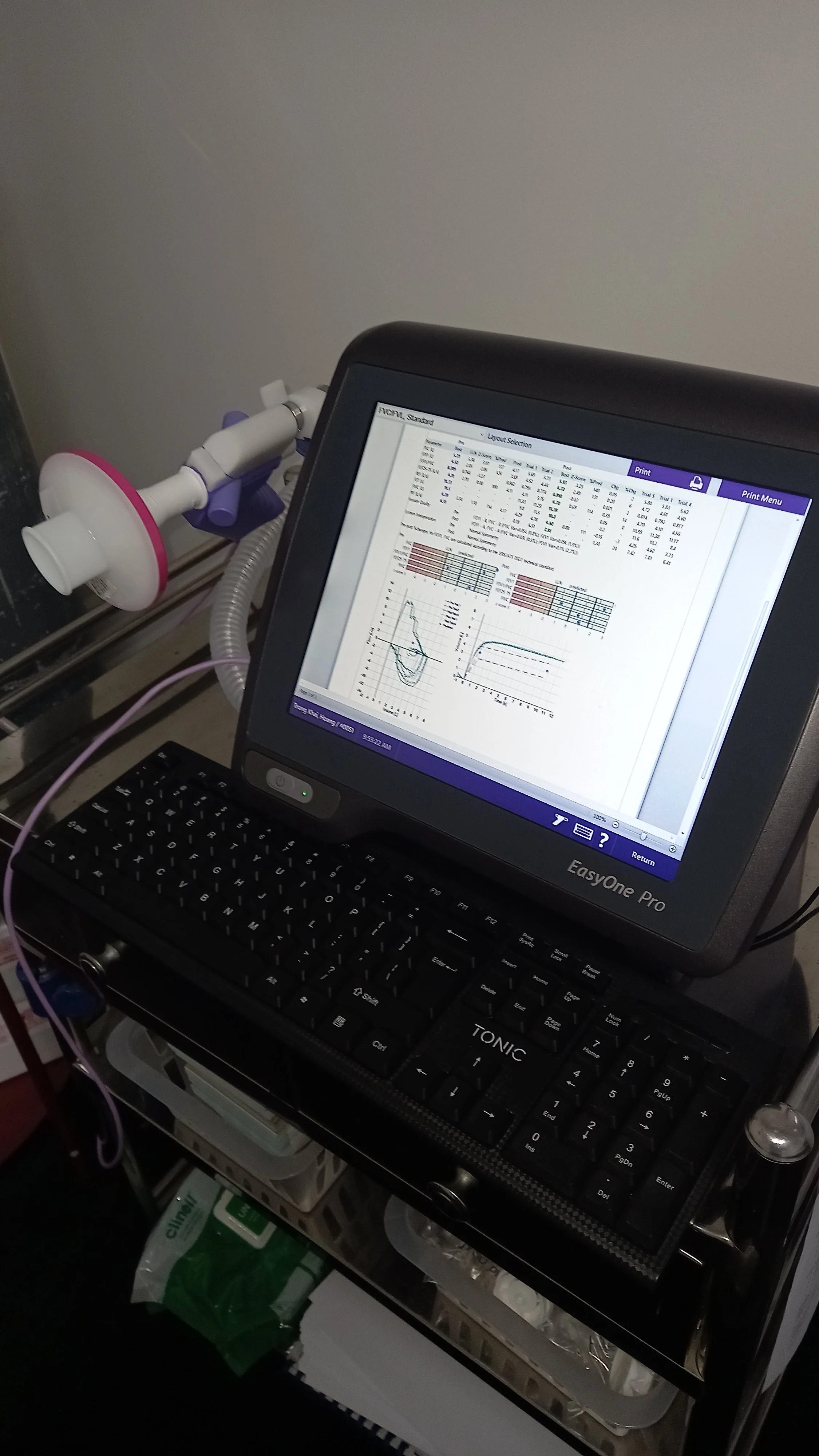 Medical desk with a computer monitor displaying graphs and tables, connected to medical equipment, on an over-the-counter cart with medical supplies underneath.