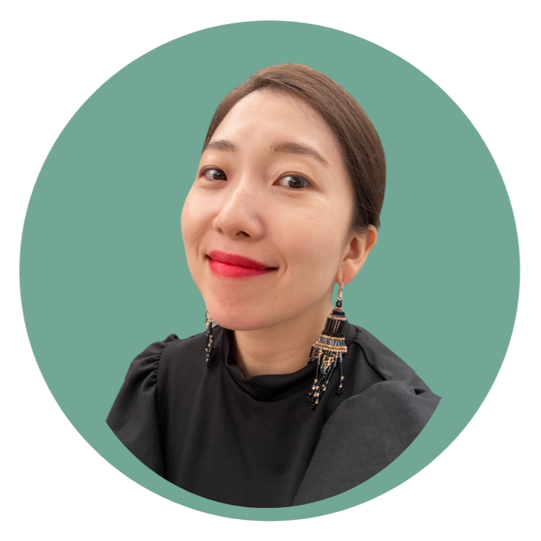 A woman smiling with red lipstick, wearing black clothing and large dangling earrings, posed against a teal circular background.