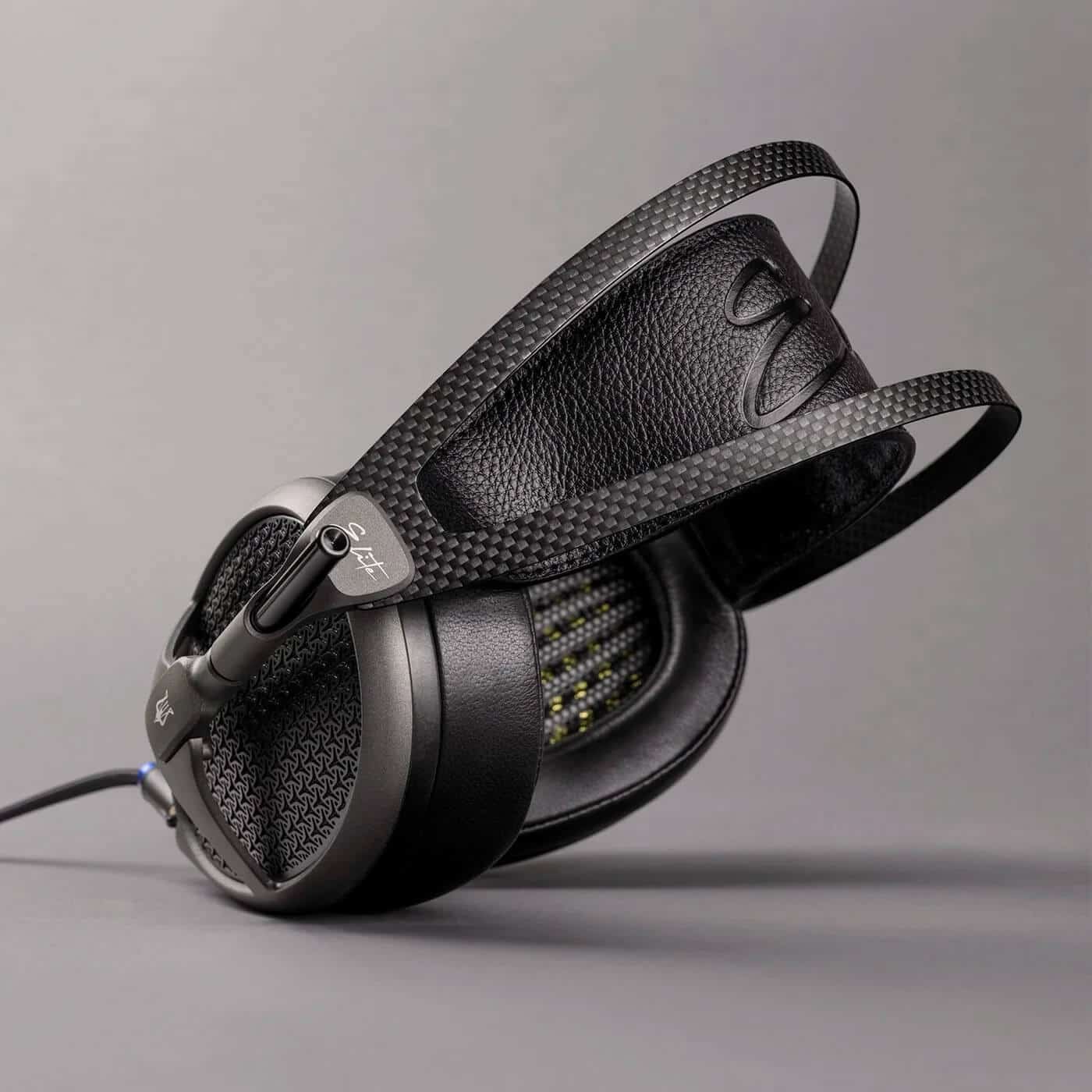 A black over-ear Meze Audio Elite headphone with a textured outer shell, leather ear pads, and a headband combined with a carbon-fibre-like material.