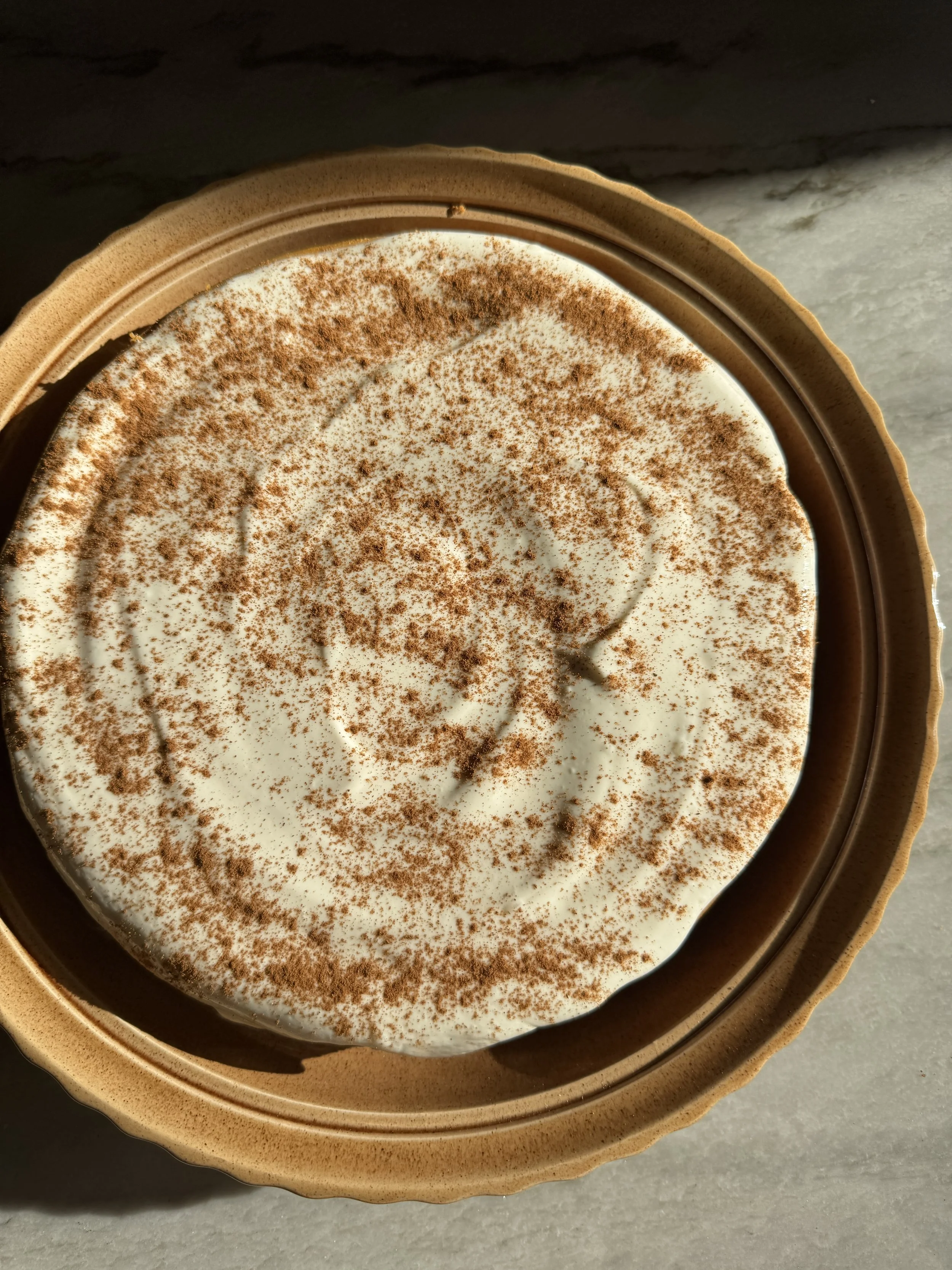 A homemade pumpkin cheesecake chilled and frosted, shown from above on a serving dish.